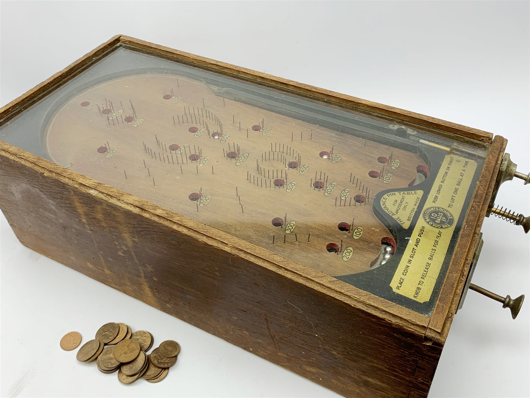 Early 20th century table top bagatelle game 'The Advance Pin Table - British Made - For Amusement Only',  in oak case with glazed top and coin operated mechanism with quantity of pre-decimal pennies 30 x 64cm