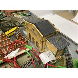 Table top 'N' gauge continental scenic layout as a split level town with various loops of track, station with numerous platforms, engine shed, assorted buildings, roads with motor vehicles and figures, tunnels, trees, river with bridge, tram depot etc 122 x 52cm