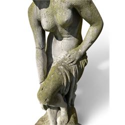 Cast stone garden figure of a classically draped nude female inspired by Aphrodite statues, with stylised up-do arranging her chitin on a circular base, the rectangular pedestal with egg-and-dart moulding over a floral wreath, in weathered finish