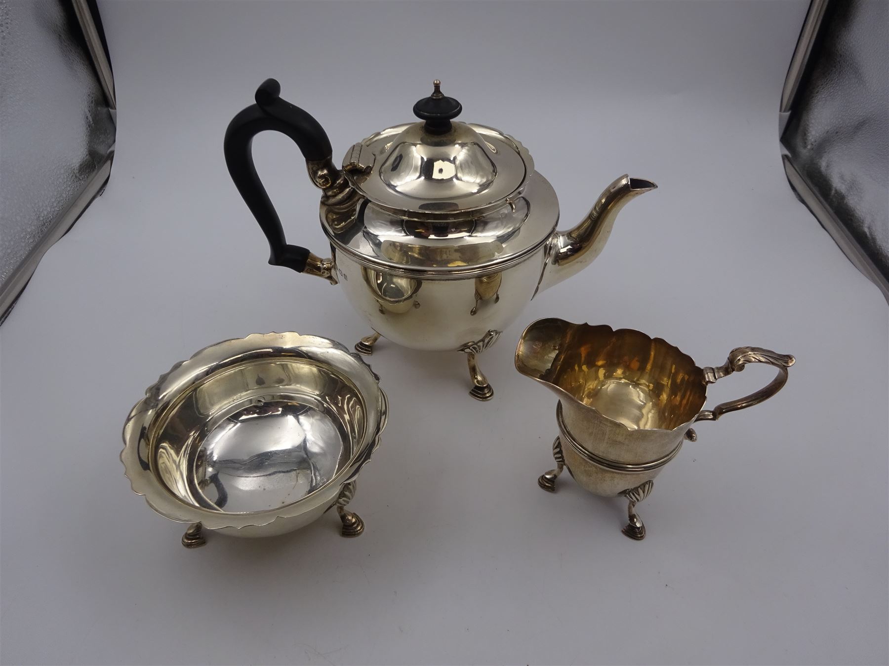 1920s three piece silver tea service, comprising teapot, with ebonised wooden handle and finial, milk jug and open sucrier, all of circular form, with shaped rims, and upon three hoof feet, hallmarked Wakely & Wheeler, London 1922, teapot H19cm