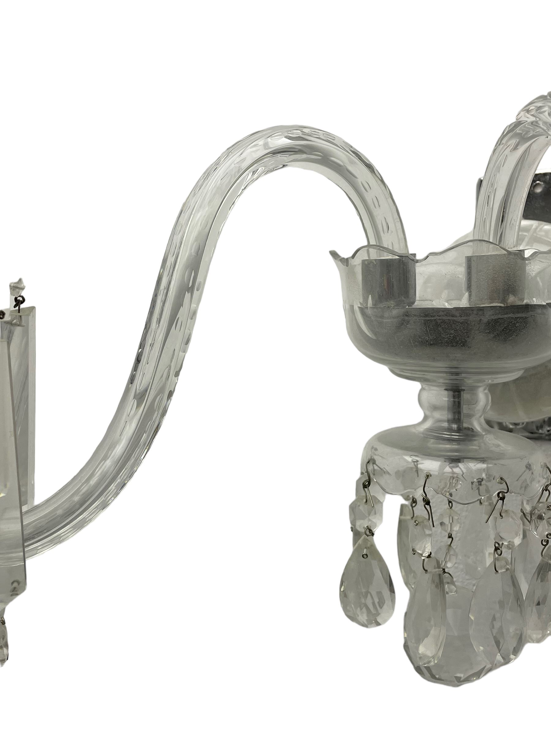 Pair of cut glass two branch wall sconce candelabras, each with S scroll extending branches with shaped and bevelled circular drip trays, hung with pendant drops