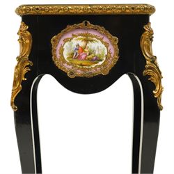 Early 20th century French ebonised sewing or work table, rectangular hinged top with foliate moulded gilt metal edge, enclosing upholstered interior, over a central Sevres style porcelain plaque depicting a courting scene, raised on cabriole supports with gilt metal carotuche and acanthus knee mounts, united by undertier with brass gallery terminating to gilt metal scroll feet