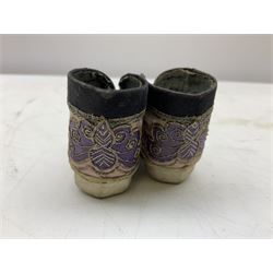 Two pairs of late 19th/early 20th century Chinese Lotus shoes for binding feet, the first with purple silk heavily embroidered with ornate floral motifs, L10cm the second larger fuschia and black pair with thicker sole embroidered with flowers, L14cm