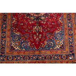 Persian Kashan hand-knotted rug, madder red ground centred by circular floral medallion with pendants, surrounded by scrolling vines, palmettes and flowerheads, dark navy spandrels, enclosed by dark navy floral border with multiple guard stripes