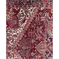 Northwestern Persian Heriz carpet, the madder red field centred by a large octofoil medallion with serrated edge, flanked by ivory stepped spandrels and geometric floral motifs in indigo, ochre and sky blue, enclosed by a navy border of rosettes and angular vines, from the region of Heriz