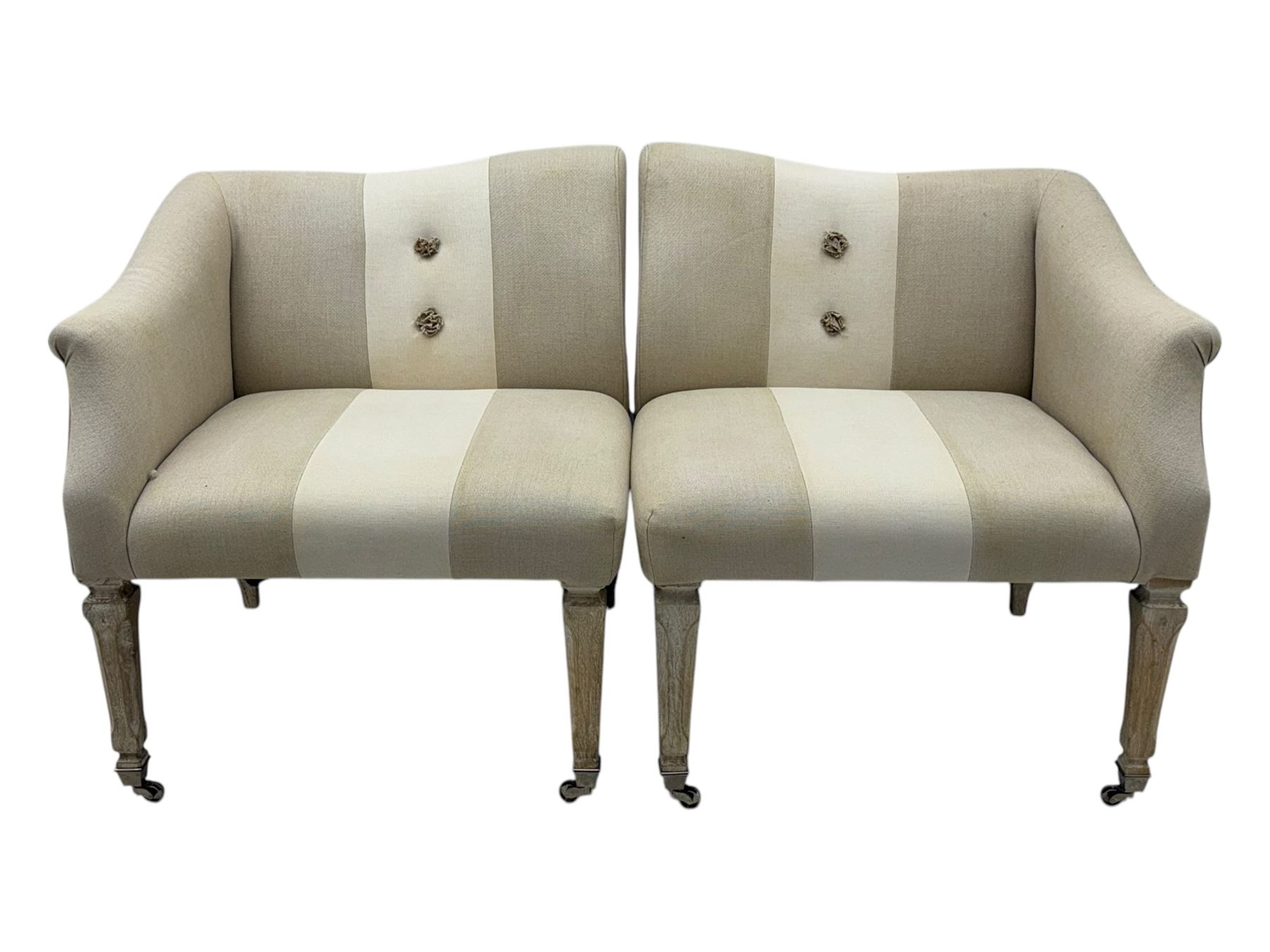 Pair of contemporary hardwood corner chairs, upholstered in broad alternating bands of neutral-toned fabric, each with two knotted rope buttons to the backrest, the whole raised on turned and lightly whitewashed supports terminating in castors