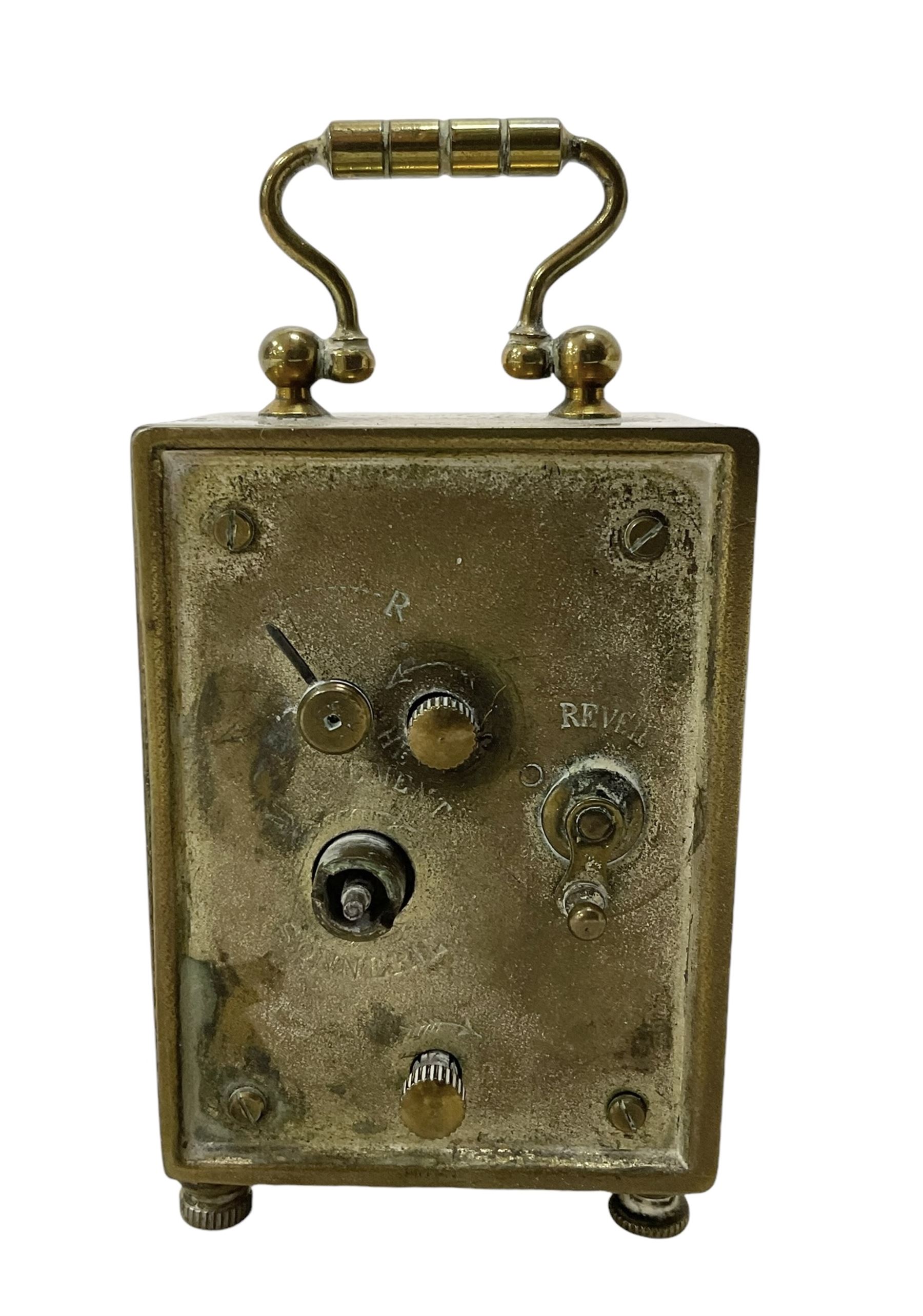 French - petite early 20th century French brass cased travelling alarm clock, with bun feet and carrying handle, circular enamel dial with Arabic numerals and spade hands, conforming alarm setting dial beneath, with a platform escapement, wound and set from the rear.