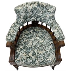 Victorian walnut framed tub-shaped armchair, the shaped rolled back supported by a spindle turned balustrade, upholstered in buttoned floral fabric, scrolled arms supports carved with acanthus leaves and flower heads, on collar turned feet with brass and ceramic castors