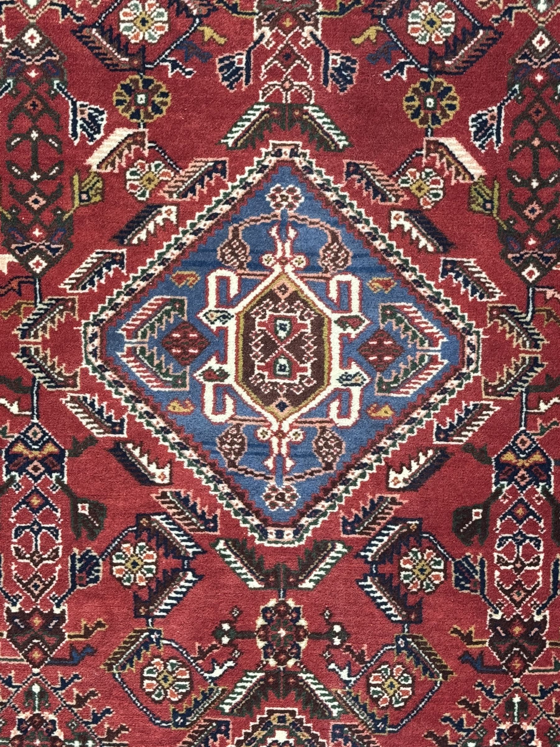 Persian Qashqai crimson ground runner, the central field decorated with three large geometric medallions with intricate angular and floral motifs, the indigo spandrels with complementary geometric designs, bordered by an ivory band with repeating floral patterns and angular vines