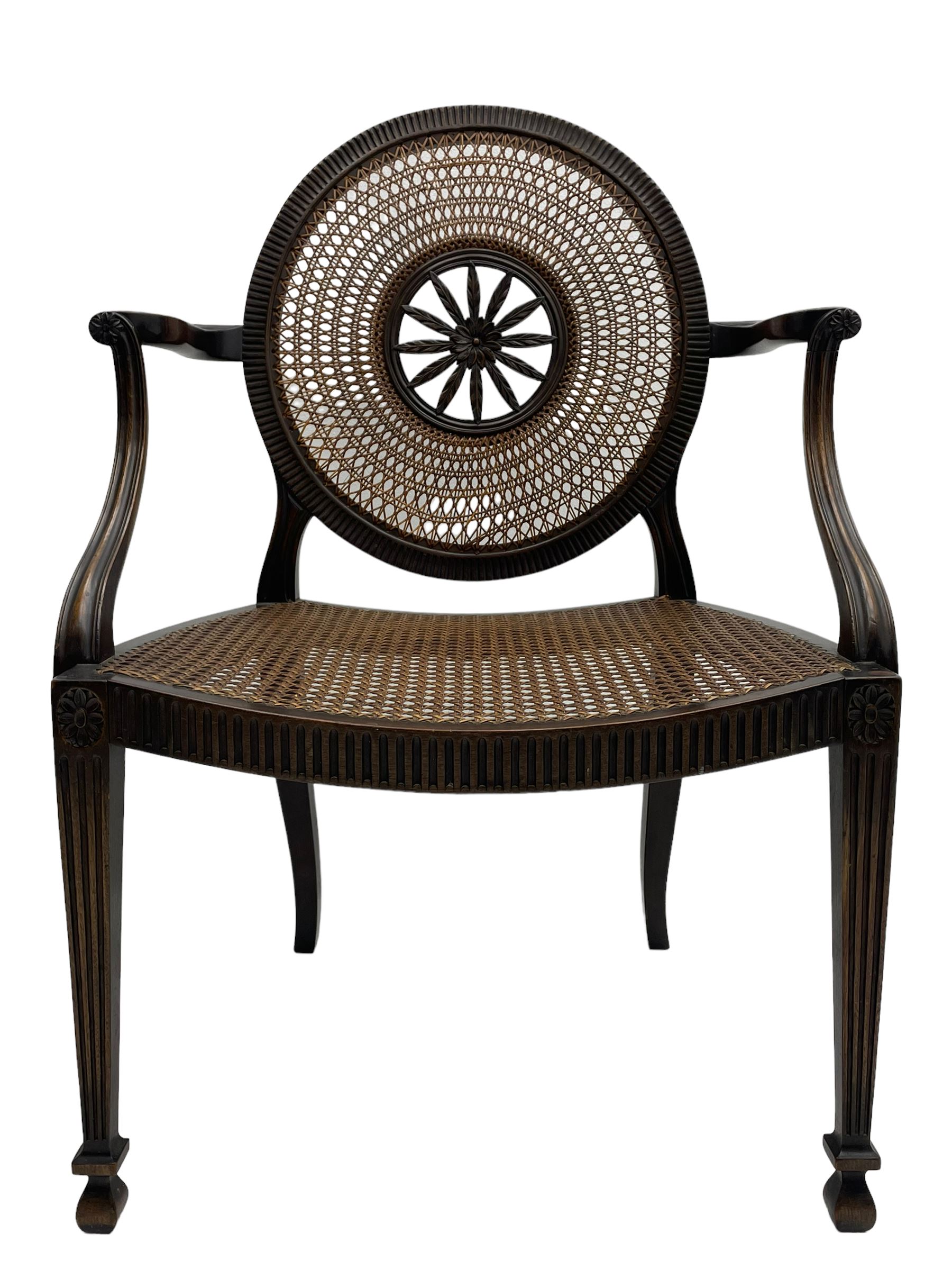 Mid-to late 20th century walnut Hepplewhite design elbow chair, circular cane back with pierced and carved central rosette, fluted frame with scrolling arms, cane seat raised on fluted rail and square tapering supports with spade feet