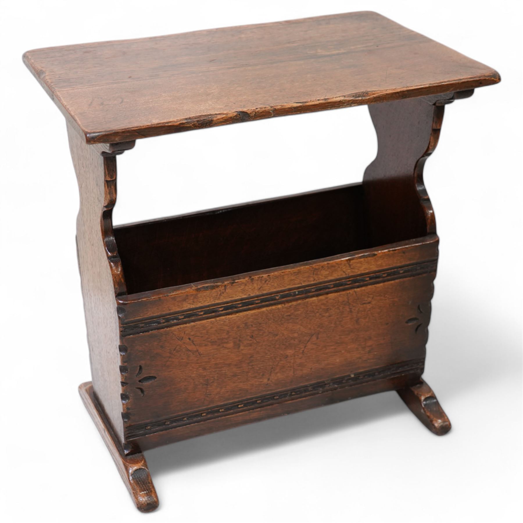 Oak magazine rack or side table, rectangular top on shaped end supports and sledge feet, panelled sides with chip carved decoration 