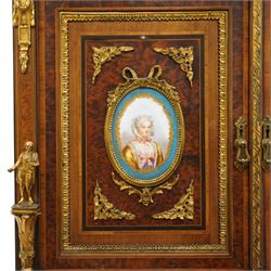 Fine late 19th century Aesthetic Movement ebony and amboyna cabinet on stand with parcel-gilt detail, the moulded cornice with pierced gilt-brass three-quarter gallery above a pair of panelled doors centred by oval porcelain portrait plaques within gilt-metal ribbon-tied frames, the doors further enriched with gilt-metal foliate mounts and flanked by classical figural terms, enclosing a shelved interior, the projecting lower section with amboyna top above a frieze drawer set with a series of floral porcelain roundels within pierced gilt-metal mounts and a central oval floral plaque, raised on turned and fluted supports with gilt-heightened detail, the mirrored back behind two amboyna shelves with pierced gilt-brass galleries, on turned feet