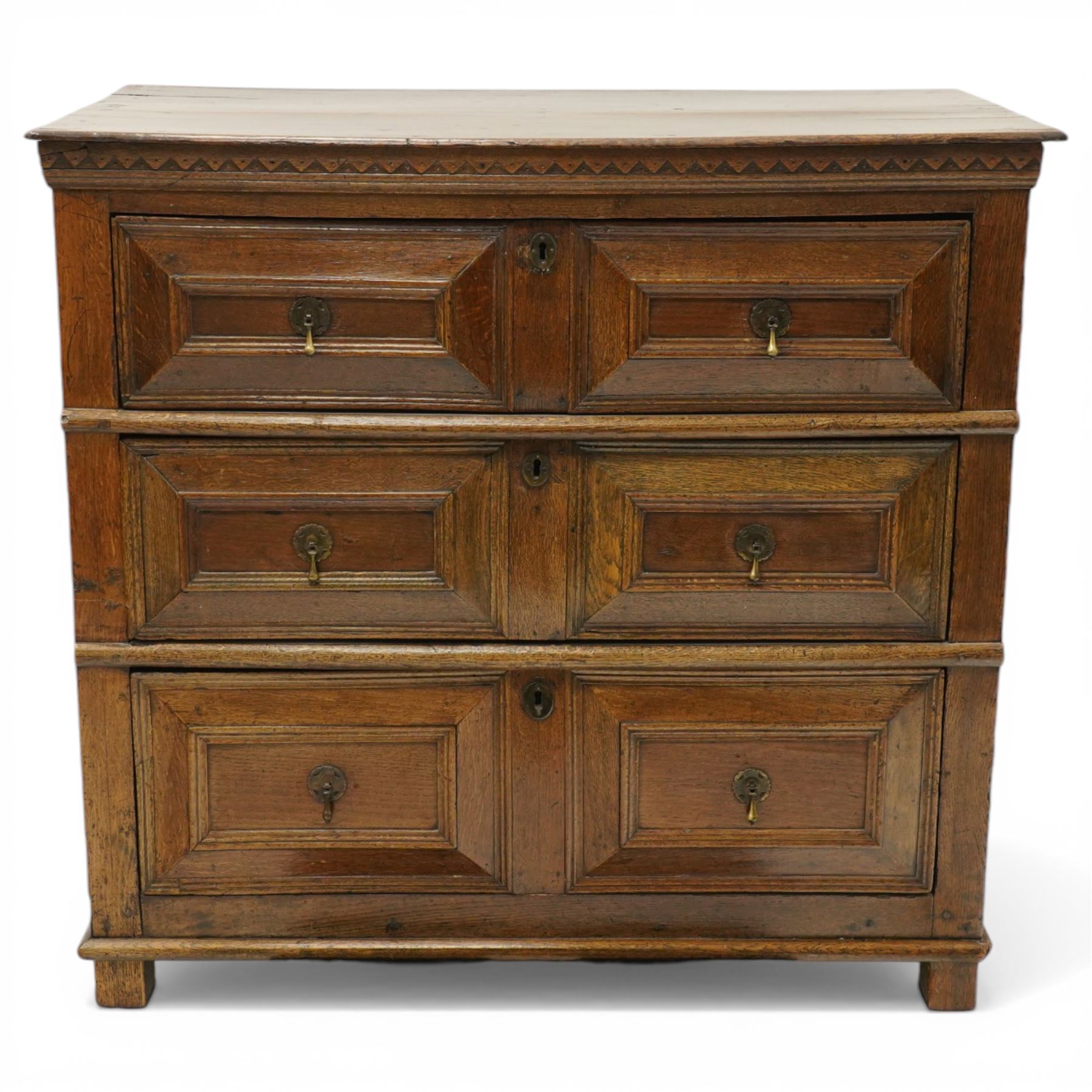 18th century oak chest of drawers, rectangular plank top with chip carved frieze, fitted with three long geometrically panelled drawers with applied mouldings, later brass drop handles, on stile supports, panelled sides and boarded back