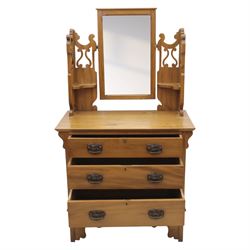 Edwardian stained pine dressing chest, the moulded top over three graduating drawers with pressed brass handles, shaped apron and bracket feet, the mirror back with rectangular plate on pivot supports, flanked by pierced Gothic style uprights with small corner shelves