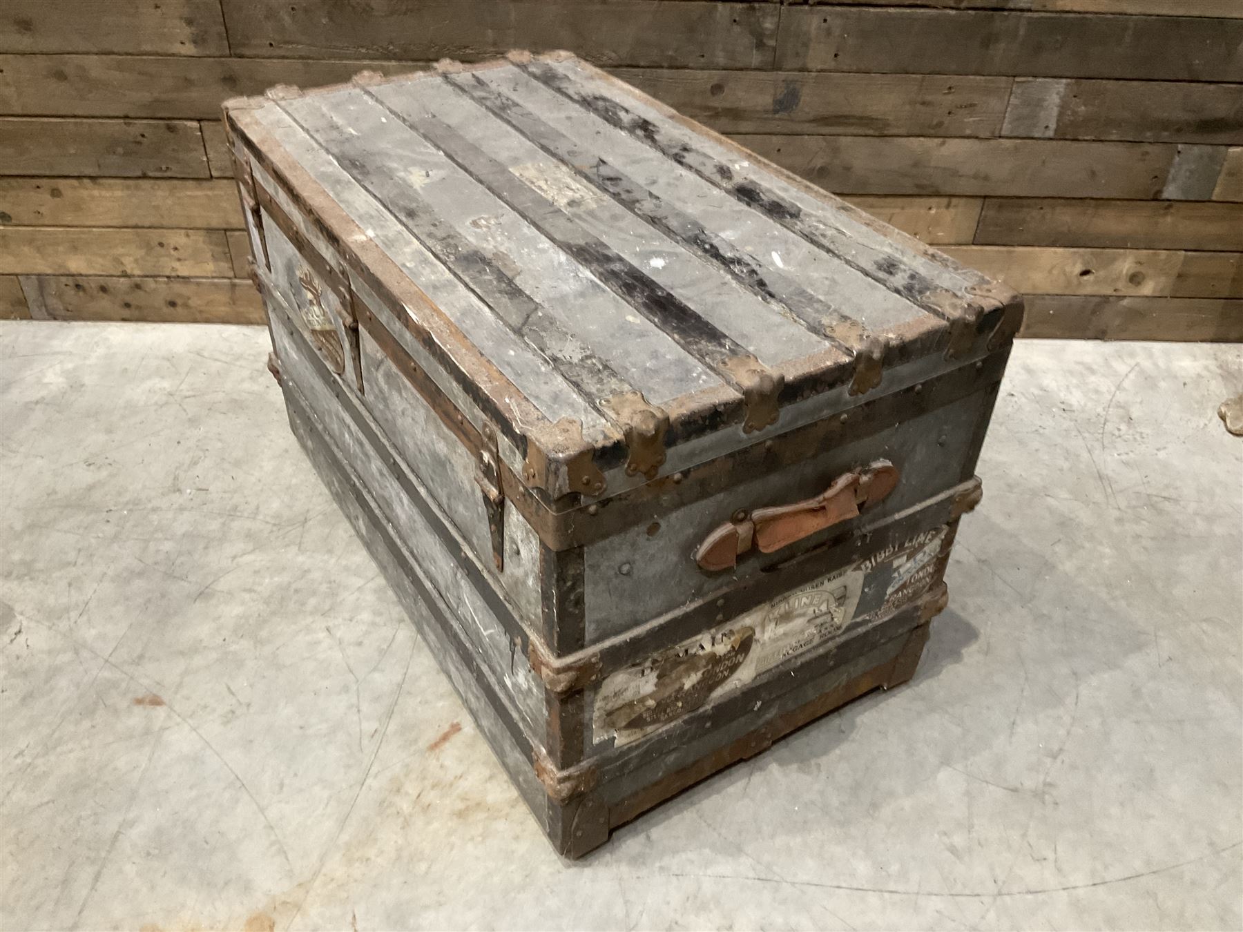 Early 20th century wood and metal bound zinc travelling trunk, hinged top with three clasps, decorated with period luggage labels