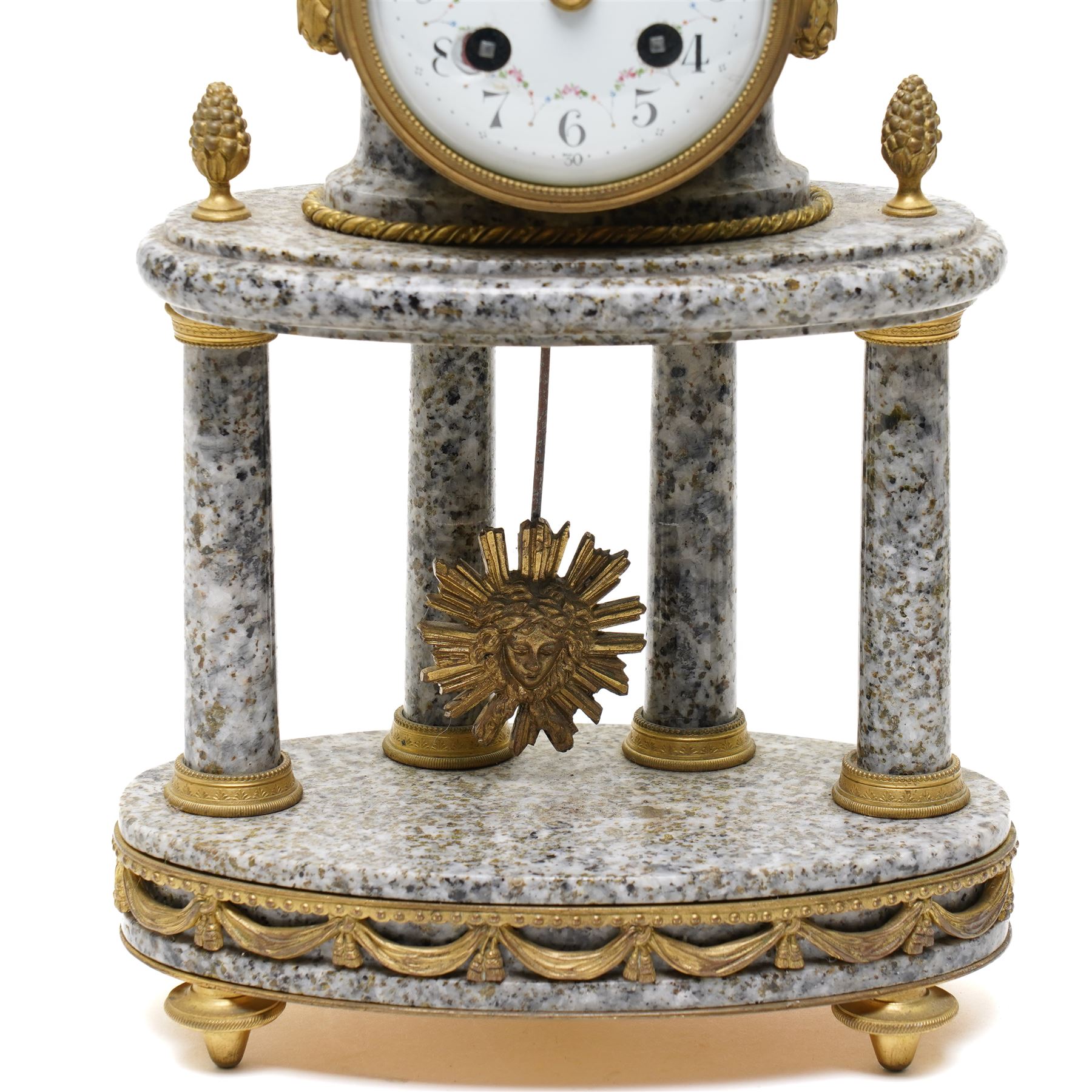 French- early 20th century portico clock garniture, 8-day drum movement decorated with laurel leaves to the glazed bezel and surmounted by a decorative urn with scroll handles, raised by four matching columns on a granite effect oval base with toupee feet, convex enamel dial with gilt pierced hands, Arabic numerals, minute markers and a garland of flowers, twin train Parisian rack striking movement, striking the hours and half hours on a bell. With a sunburst pendulum and key and a matching pair of two-light candelabra.
