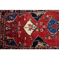 Persian Hamadan runner rug, the vermilion ground decorated with a row of ivory and indigo medallions interspersed with stylised flowering plants, indigo spandrels, enclosed by an indigo floral border and narrow patterned guard stripes