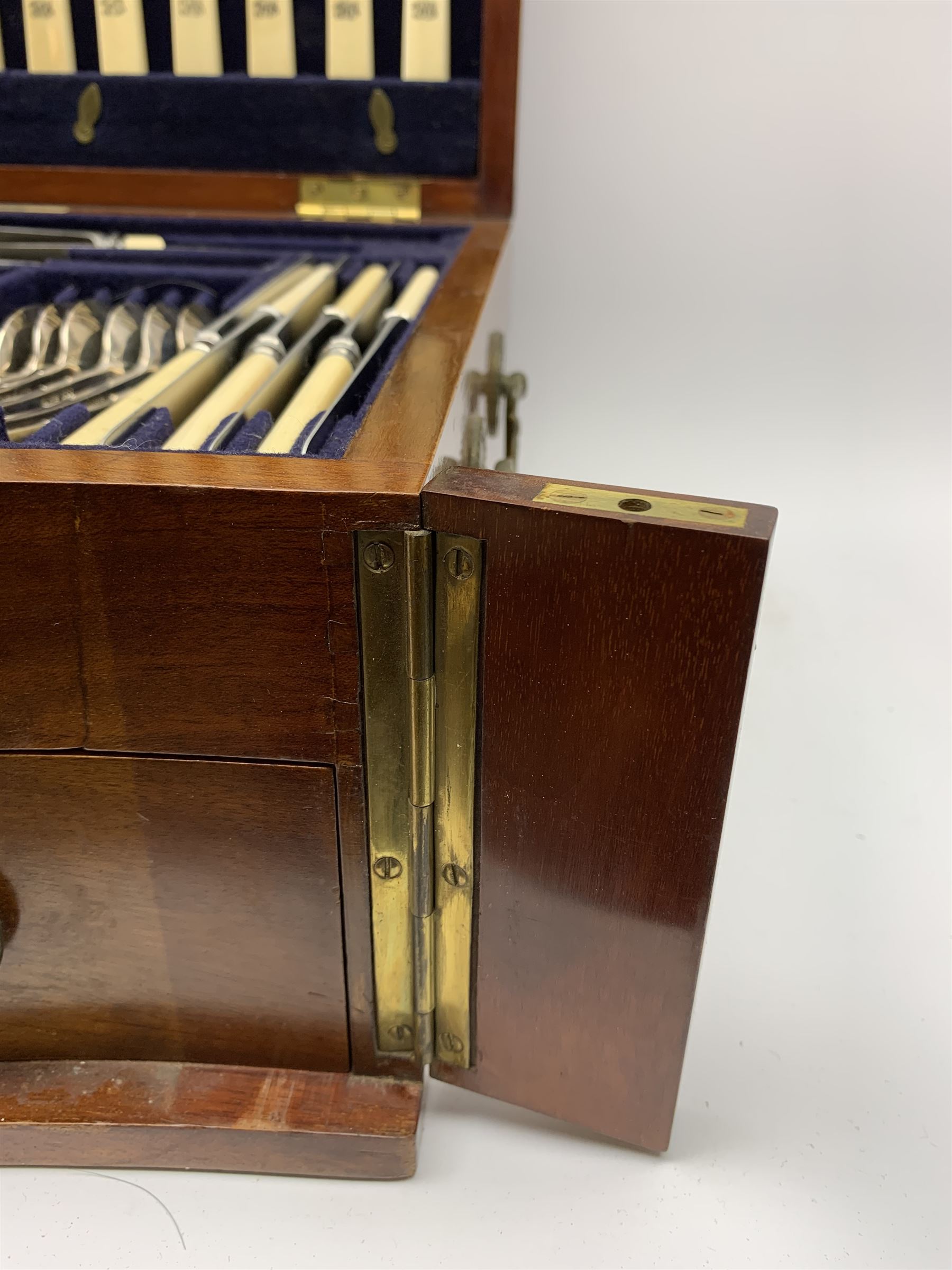Late 19th/early 20th century composite canteen of silver flatware, contained within an early 20th century mahogany serpentine fronted case with twin drop carry handles, and hinged cover with boxwood stringing and central inlaid shell motif, above a single drawer with twin ring handles and Wellington style locking system, the cover and drawer opening to reveal plaque for Spink & Sons Ltd London, and fitted interior containing ivory handled knives, ivory handled carving set, and silver Hanoverian and Old English pattern cutlery, each with engraved monogram to terminal, hallmarked London, makers Spink & Son (John Marshall Spink), Goldsmiths & Silversmiths Co, and Chawner & Co (George William Adams), various dates ranging 1880-1923, gross weighable silver 92.59 ozt (2880 grams)