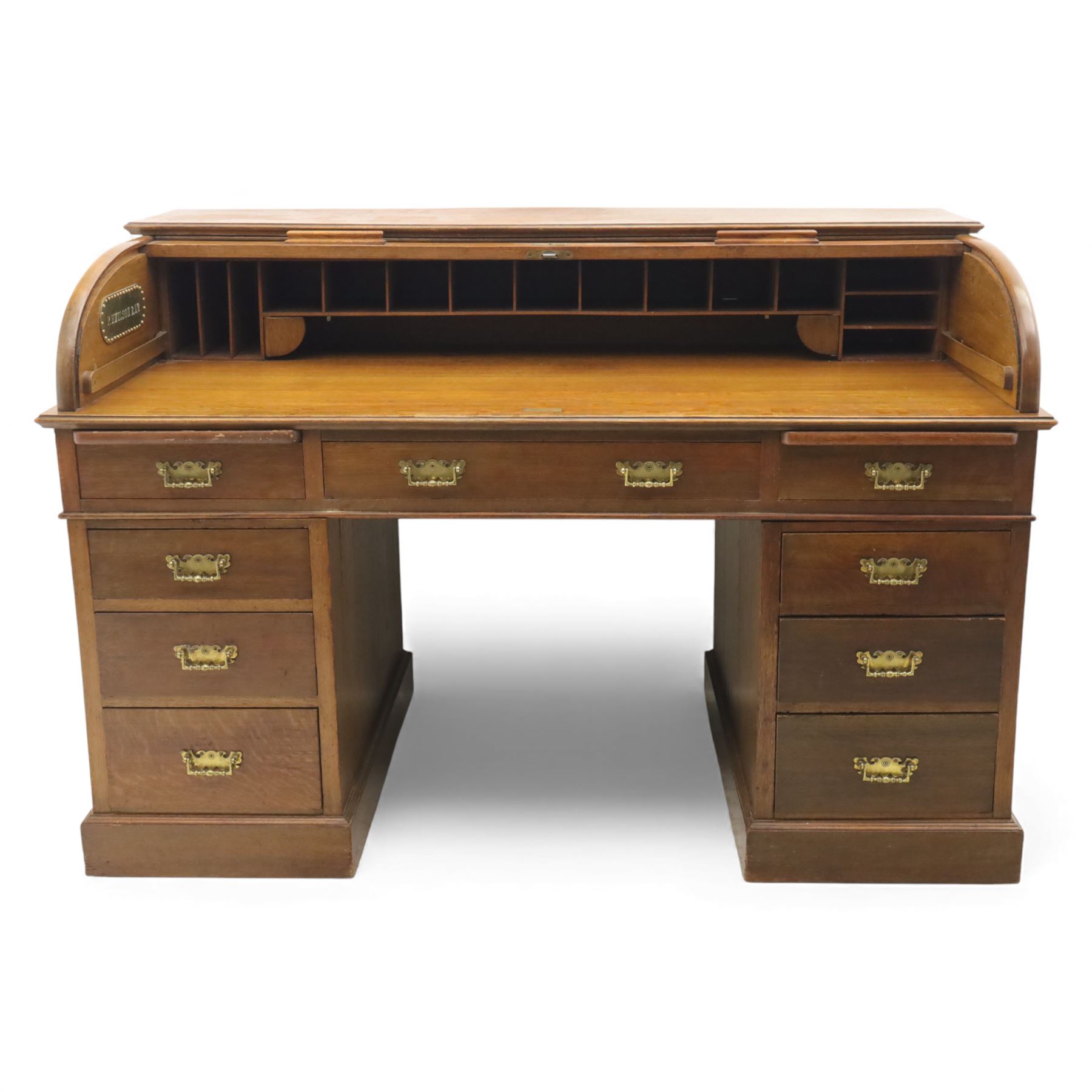 Edwardian oak roll-top desk, the tambour enclosing a fitted interior of pigeonholes and dividers, over a central kneehole flanked by twin banks of drawers with brass handles, on plinth bases