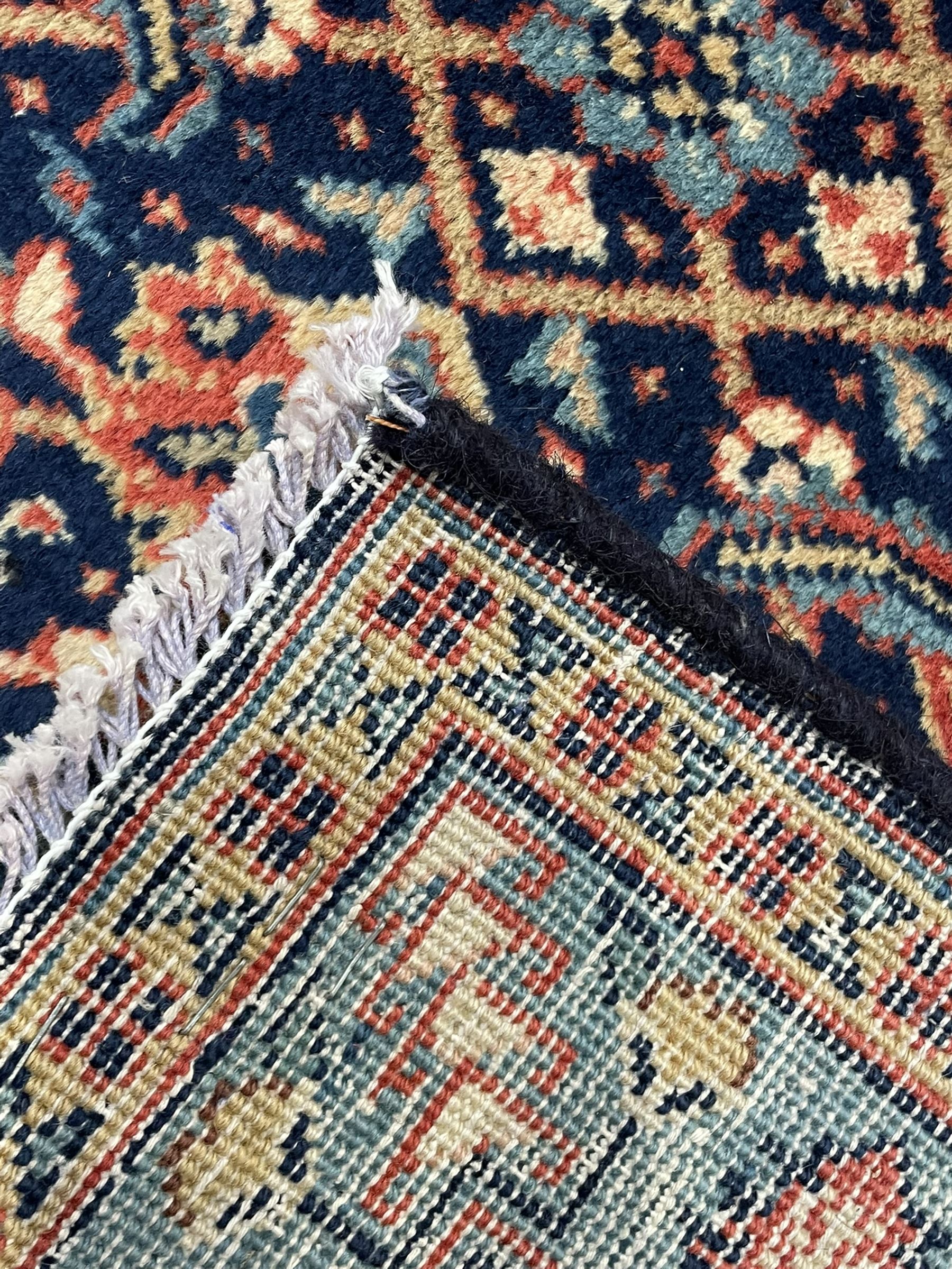 Persian Heratti indigo ground carpet, the busy field decorated with repeating floral pattern Heratti motifs, scrolling leafy branches and palmettes to the crimson ground border, within foliate pattern guard stripes 