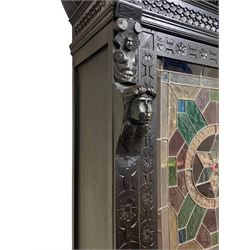 19th century heavily carved and stained oak cabinet on cupboard, the projecting moulded cornice over gadroon carved frieze, the upper cabinet enclosed by stained and leaded glass door in geometric pattern with central star motif, in various coloured and textured glass panes, the upright rails carved with flower heads and the panelled back carved with circular motifs behind turned supports, moulded rectangular top over frieze drawer and cupboard, the cupboard enclosed by panelled door carved with Flemish design tavern scene, moulded skirted base on block feet
