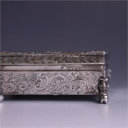 Victorian silver tobacco box, rectangular form, hinged lid embossed with a gaming scene, the body engraved with scrolls and flowers, upon four scrolling mask feet, hallmarked George Heath London 1885, H4.5cm, W10.5cm