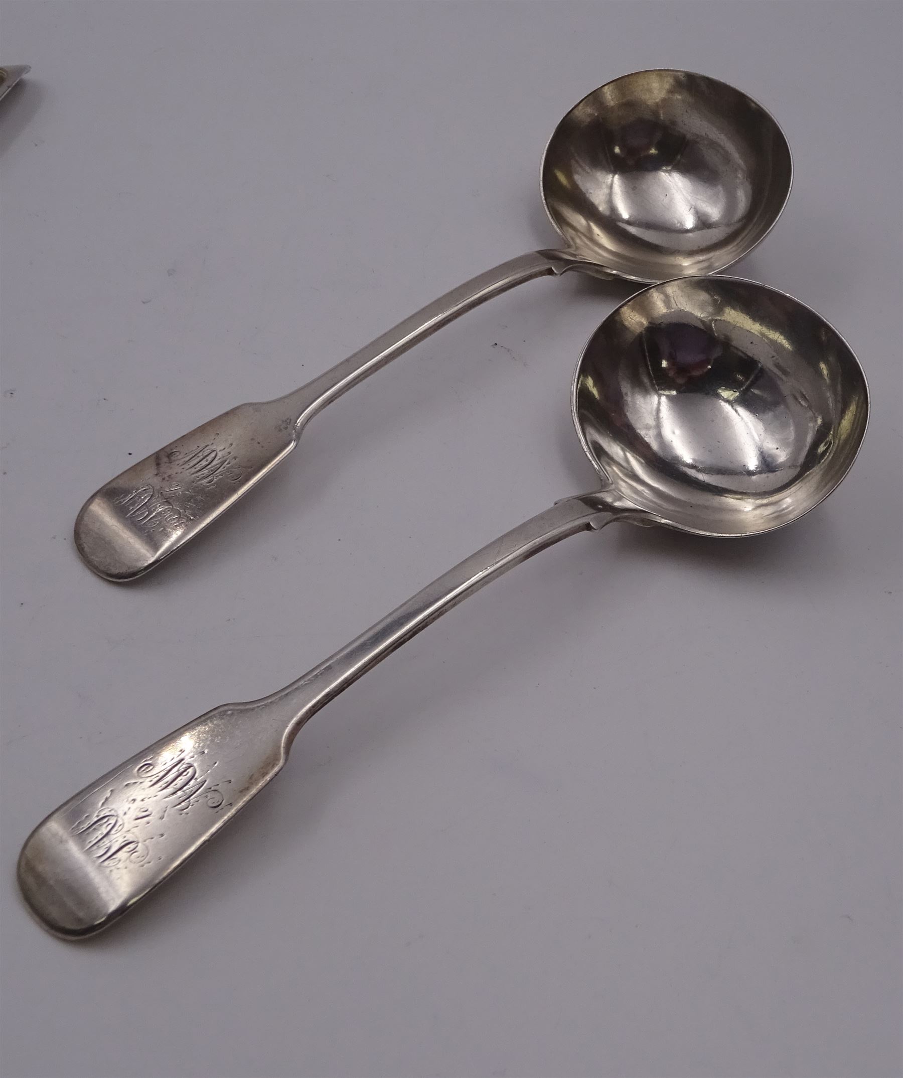 Group of Victorian silver fiddle pattern spoons, comprising pair of sauce ladles and set of six teaspoons, both hallmarked Henry Holland (of Holland, Aldwinckle & Slater), London 1857, set of four table spoons, hallmarked Chawner & Co (George William Adams), London 1857, and set of six dessert spoons, hallmarked Chawner & Co (George William Adams), London 1856, with monogrammed terminals, approximate total silver weight 25.50 ozt (792.6 grams)