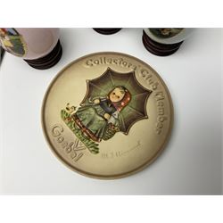 Two ceramic Hummel postcards by Goebel, both displayed on wooden easels, together nine Hummel eggs, set of four Hummel School Days plates, on wooden hanging rack, Goebel Collectors Club Member plaque etc