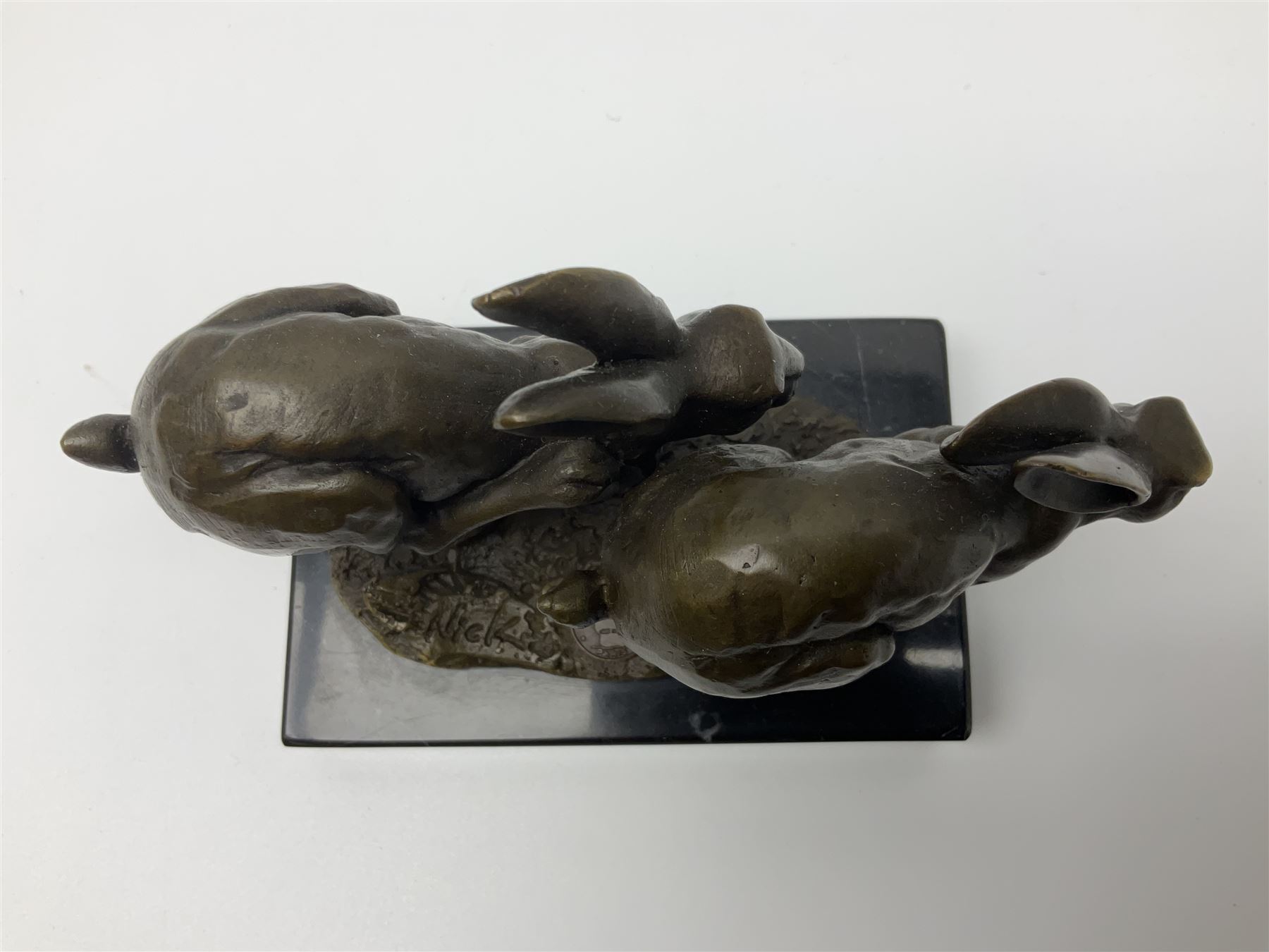 Bronze figure group, modelled as two hares in chase, upon a naturalistic base signed Nick and with foundry mark, raised upon a rectangular marble base, overall H12cm. 