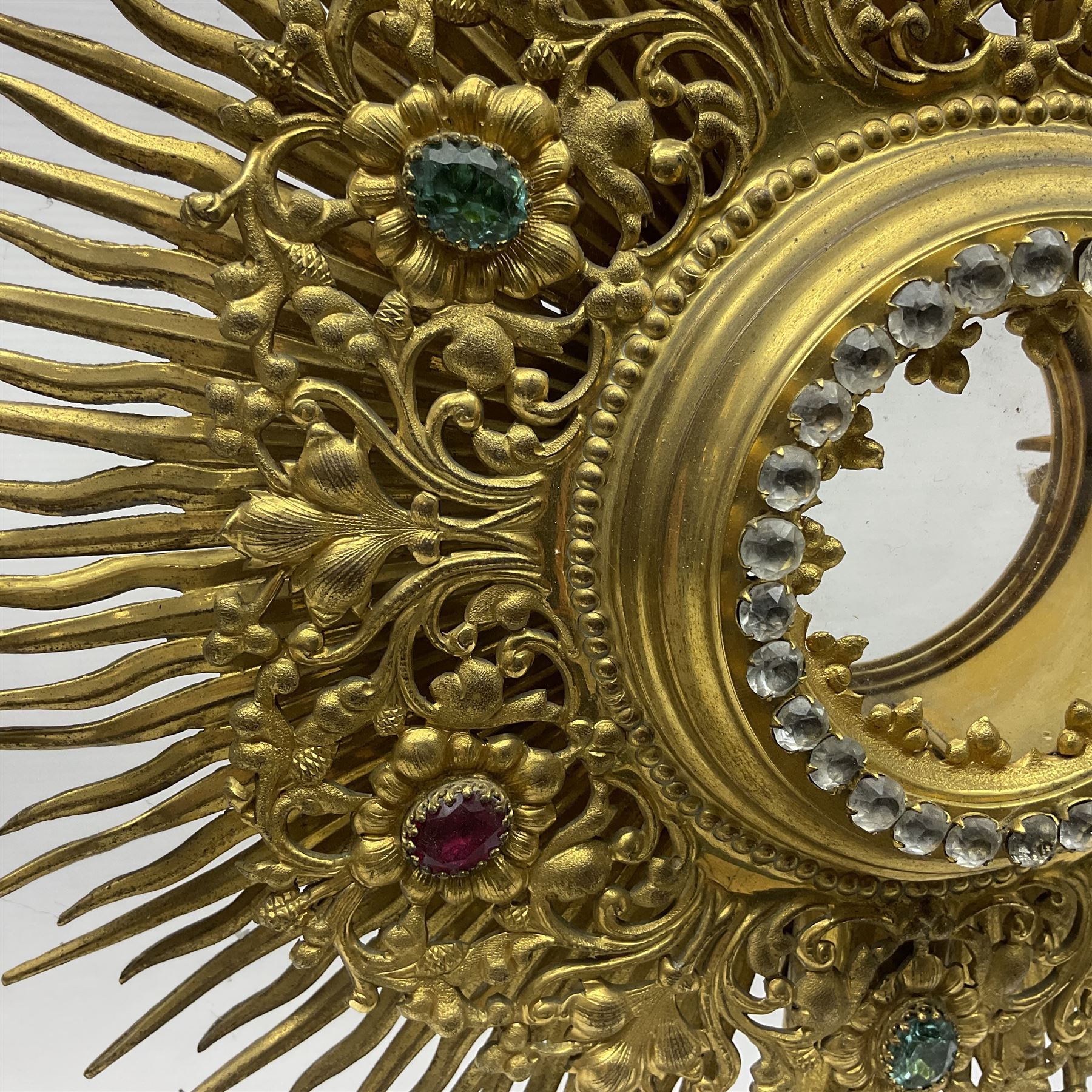 20th century gilt metal monstrance, in the Gothic revival style, with glazed aperture to centre surrounded with clear paste stones, in a pierced floral and scroll border set with coloured paste stones, within a sunburst surround, on a paste set knopped stem and similar foliate foot, H59.3cm