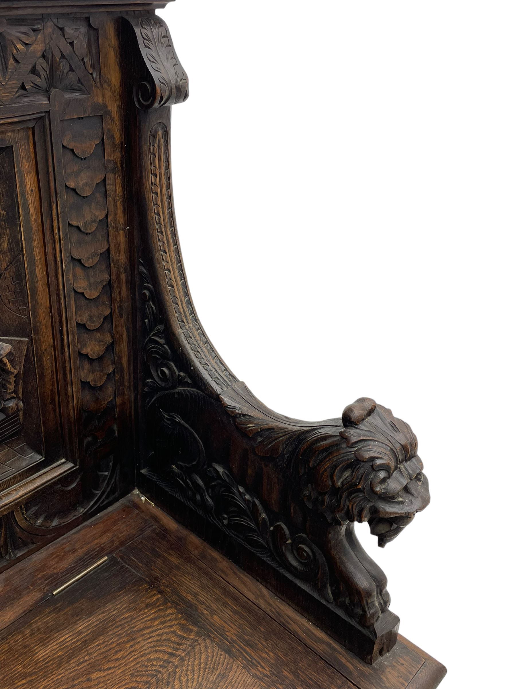 19th century heavily carved oak settle, the moulded upper rail over triangular foliage carved frieze, three Flemish style carved panels depicting tavern scenes, acanthus carved uprights terminating to lion carved arms, hinged box seat, the panelled front carved with lion masks and extending scrolled acanthus leaves, on moulded skirt base