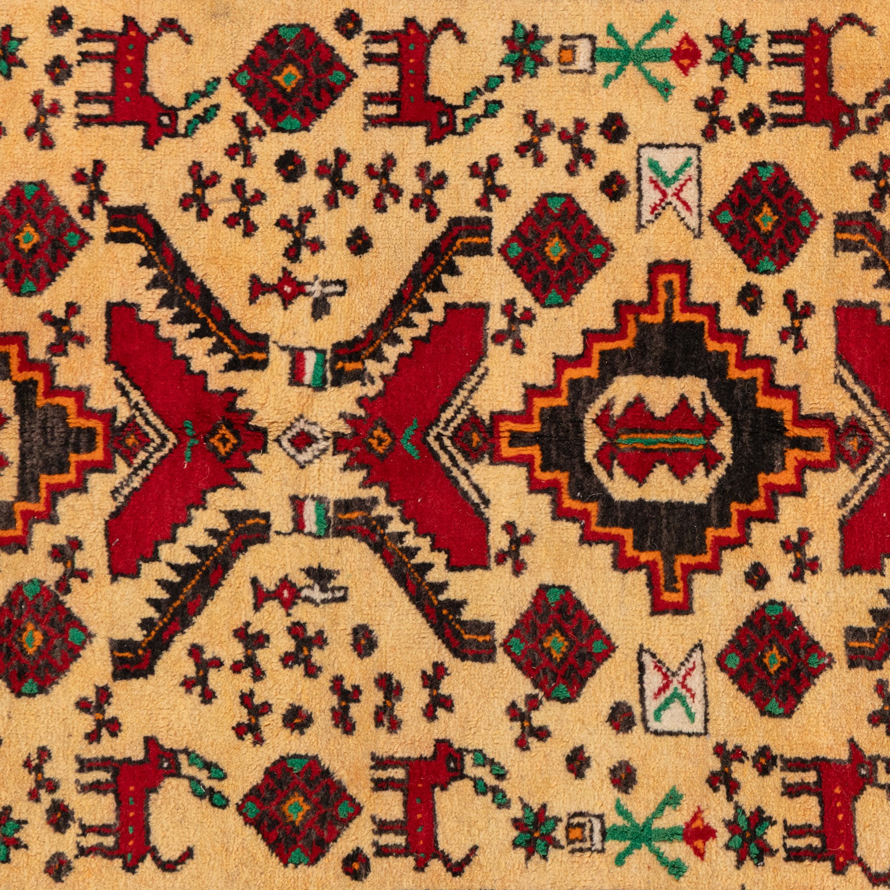 North East Persian Meshed Baluch rug, the ivory field decorated with two stepped diamond medallions and angular red motifs, interspersed with stylised horned animals, birds, flowerheads and geometric devices, enclosed by a dark brown border of repeating red serrated leaves and narrow ivory guard bands