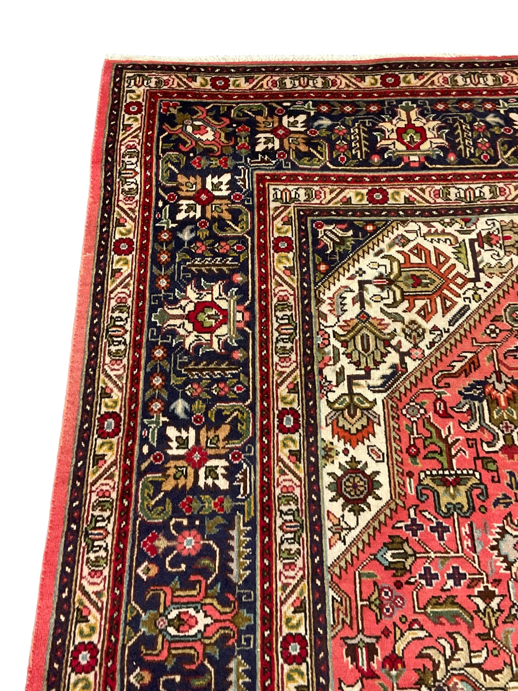 North West Persian pink ground Tabriz carpet, central indigo ground medallion surrounded by stylised plant motifs and trailing foliage, the main border with overall floral design within guard stripes 