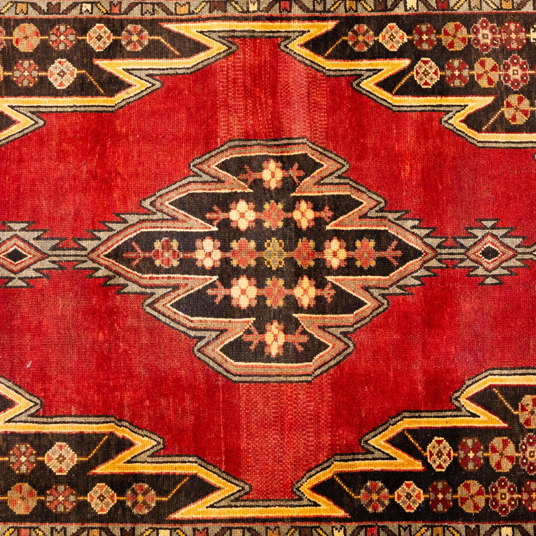 West Persian Mazlaghan hand-knotted rug, madder red field with central stepped lozenge medallion with pendant motifs flanked by angular serrated spandrels filled with small geometric devices, enclosed within multiple borders featuring stylized floral and geometric motifs, with cotton fringe ends 