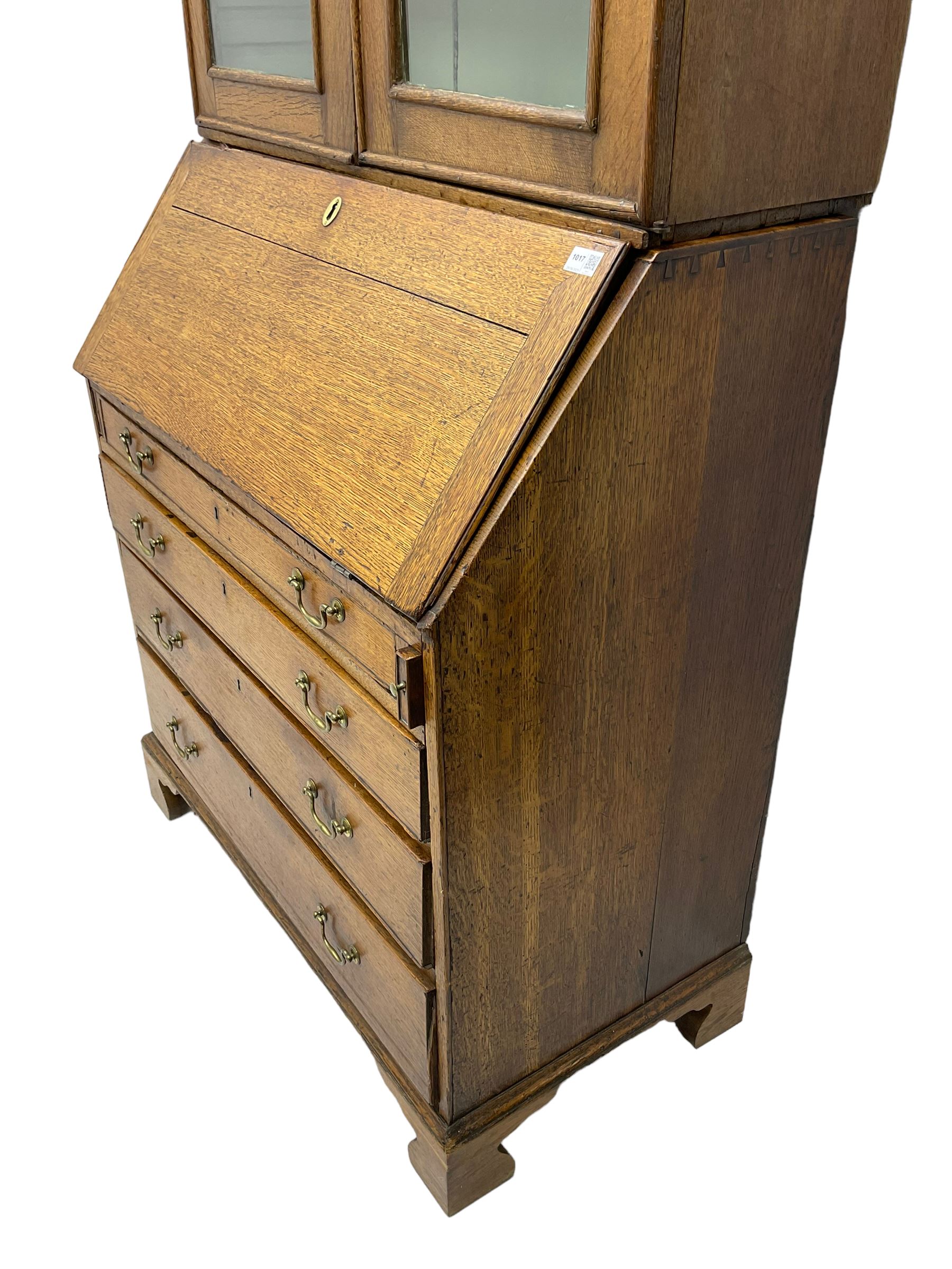 George III oak bookcase on bureau, the double arched top enclosed by two shaped glazed doors, fall-front concealing fitted interior, over four graduating cock-beaded drawers, on bracket feet