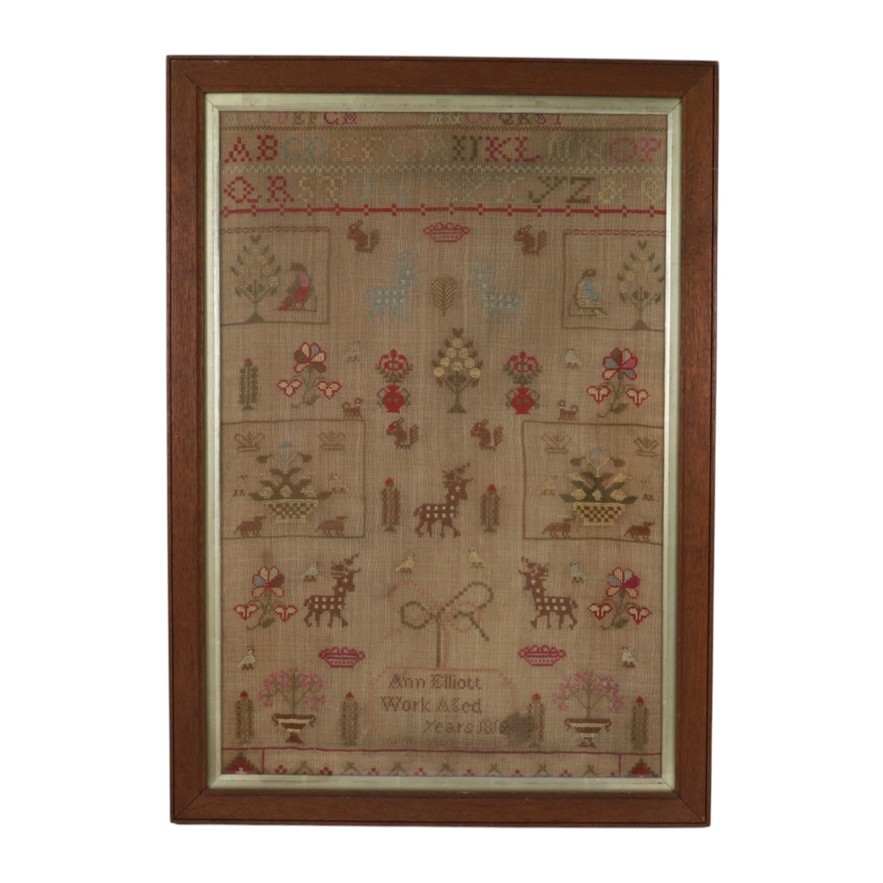 Early 19th century sampler, by Ann Elliott, 'Work Aged', dated 1819, worked with alphabet band above various motifs including squirrels, crown, stags, flowering urns and birds, including frame 73cm x 52cm