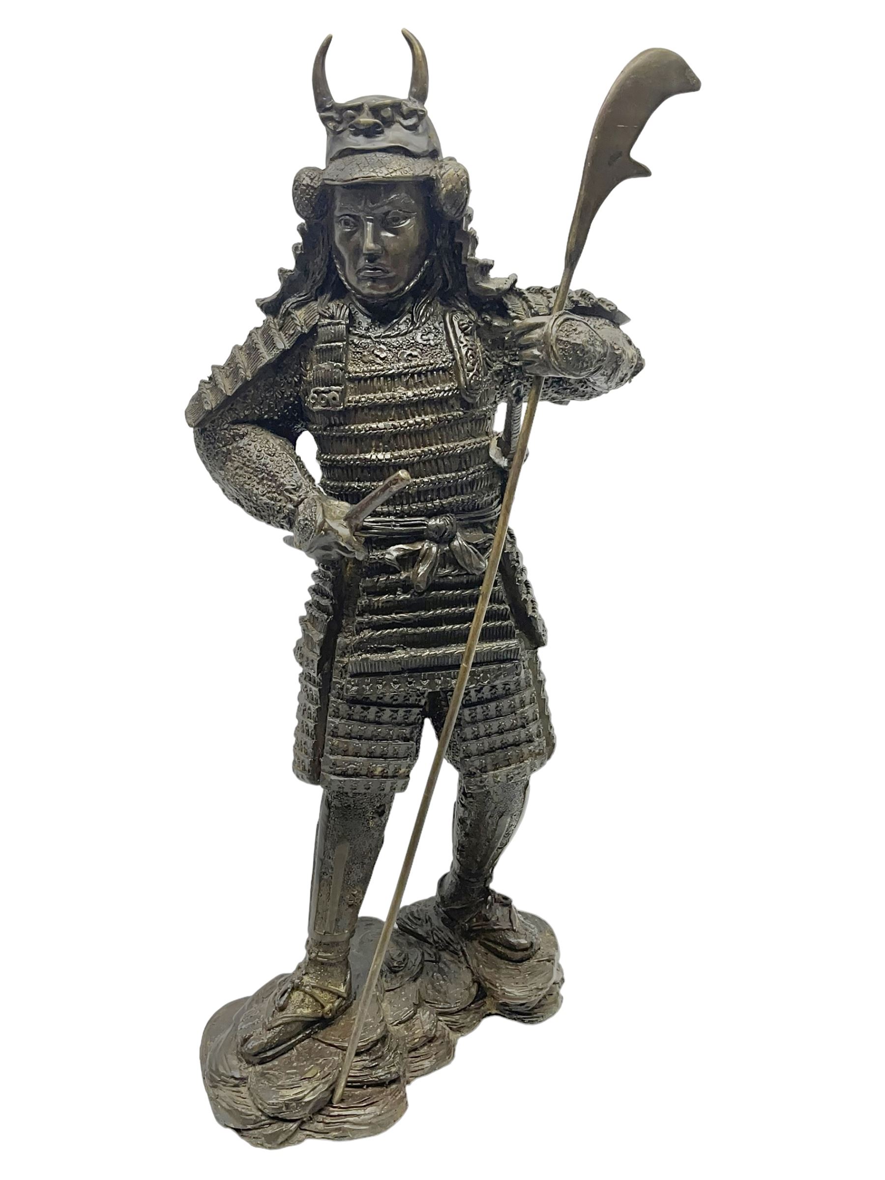 Bronze figure of a samurai standing wearing armour and holding a naginata, upon a rocky base, H48cm