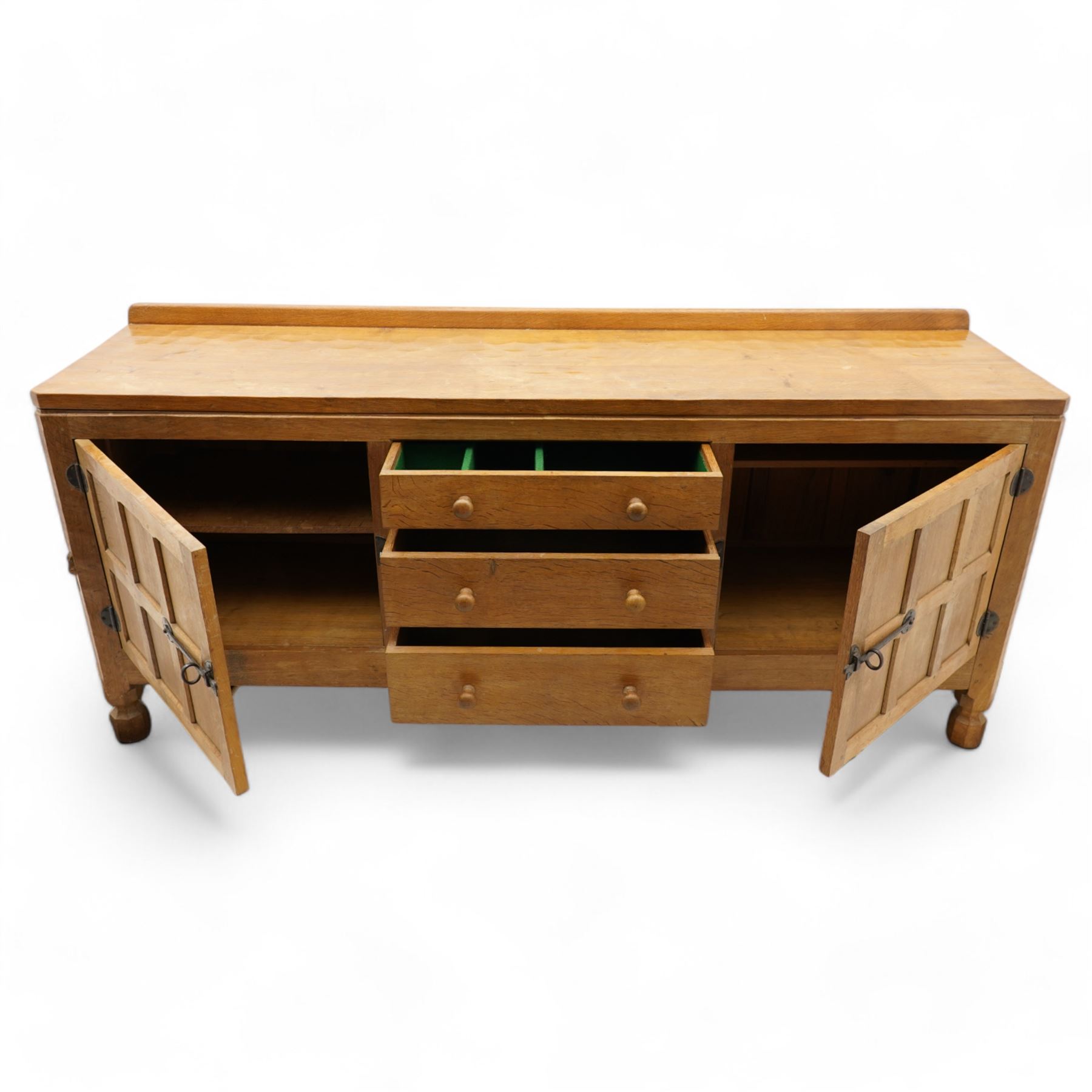 Mouseman - adzed and panelled oak 6' sideboard, fitted with four central drawers and flanking cupboards, enclosed by two panelled doors with wrought metal latches and hinges, on octagonal feet, carved with mouse signature, panelled sides, by the workshop of Robert Thompson, Kilburn 