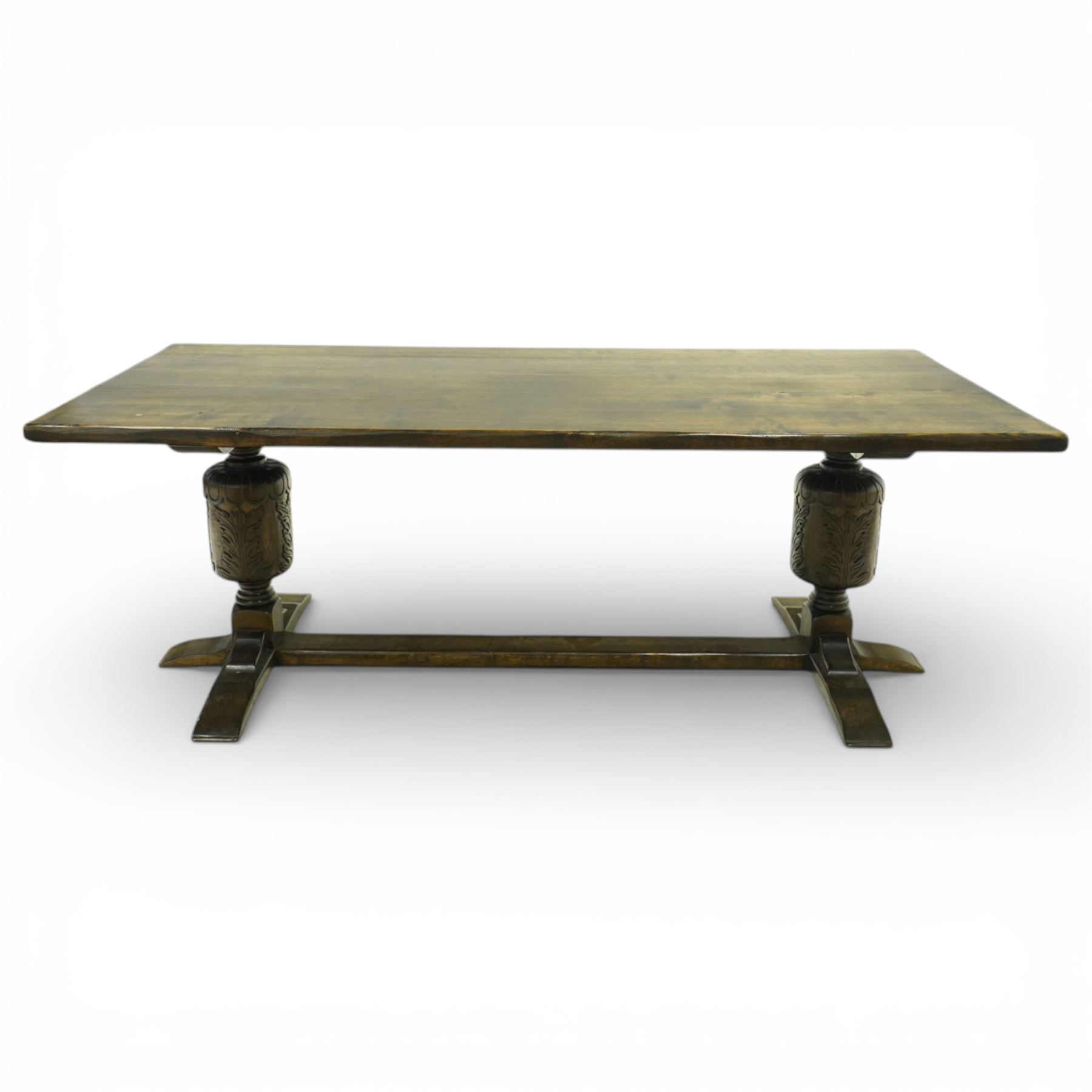 20th century oak refectory style dining table and eight chairs (6 + 2), rectangular top on two large carved baluster pedestal supports with leaf decoration, on splayed trestle bases joined by a stretcher, with eight matching oak dining chairs, each with Yorkshire rose carved cresting rail, panel back and solid seat, raised on turned supports united by stretchers