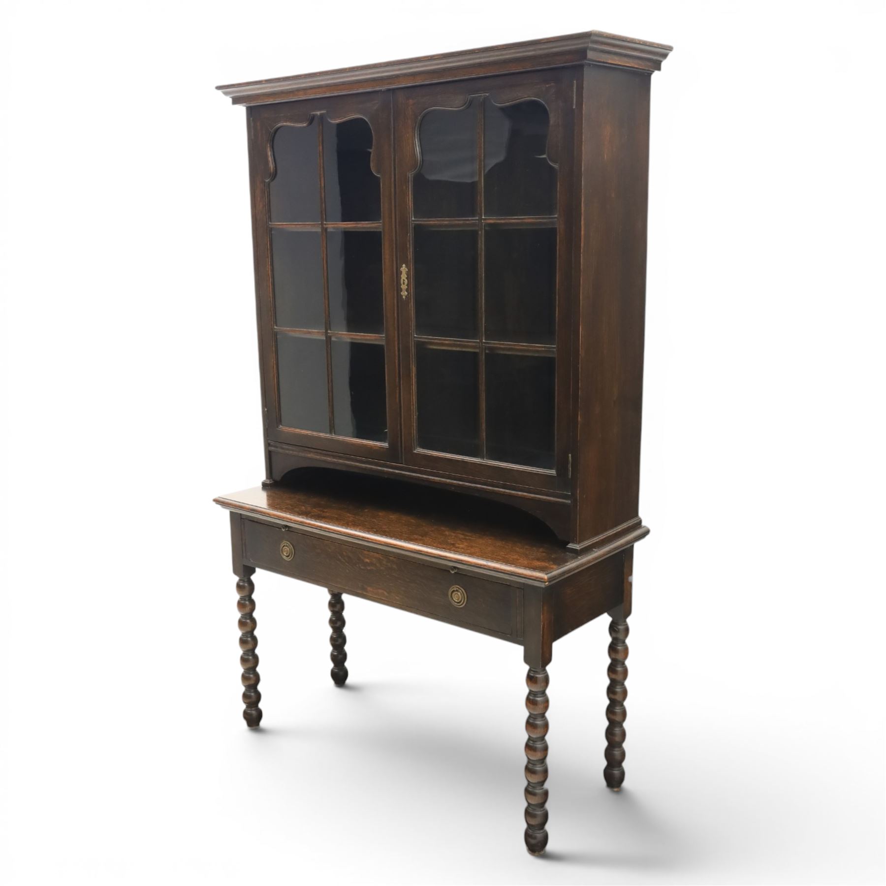 Early 20th century Jacobean Revival dark stained oak dresser, the associated upper section enclosed by twin glazed doors with shaped moulded glazing bars, over separate base fitted with two drawers, raised on bobbin turned legs