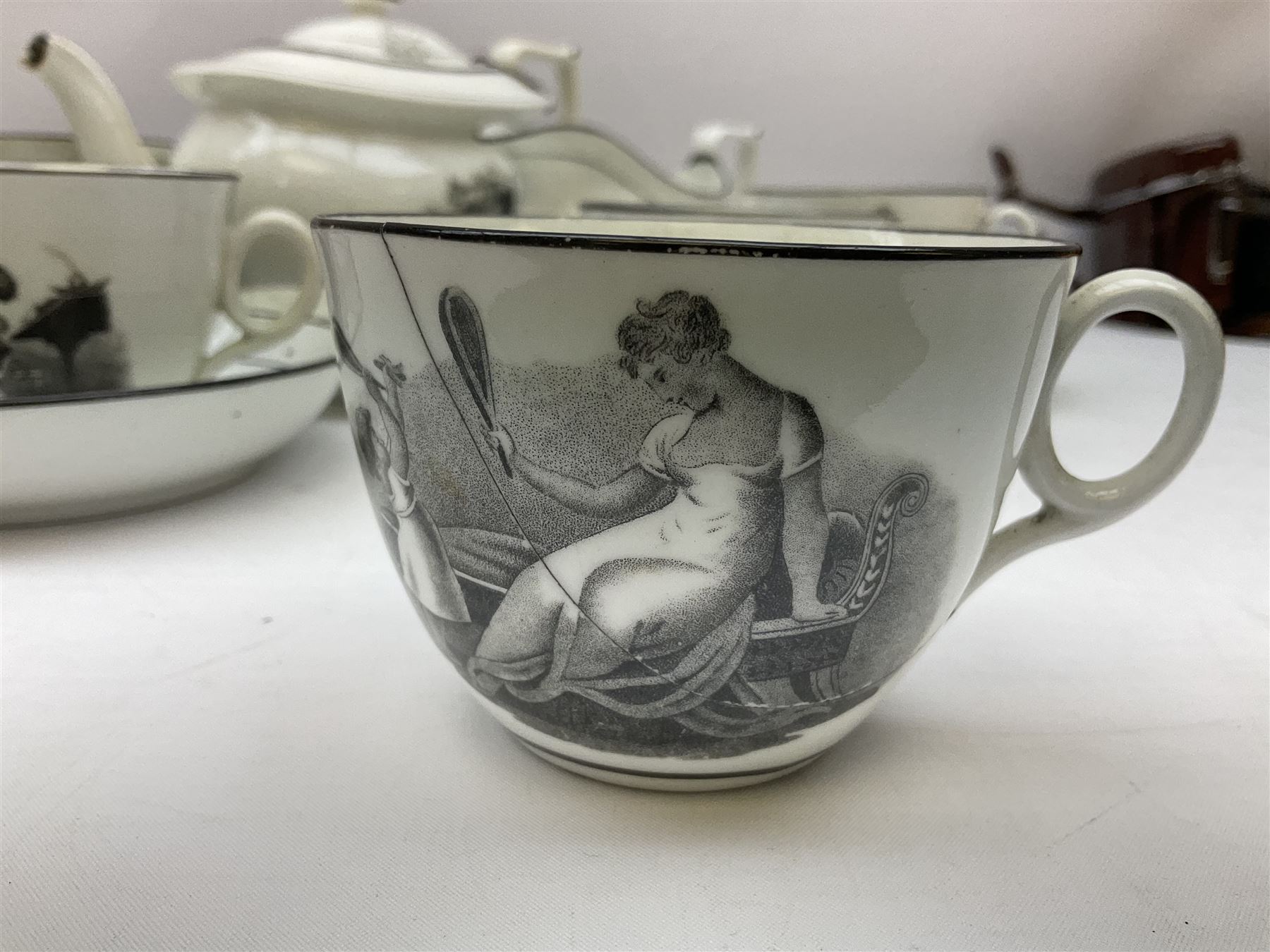 Early 19th century Staffordshire bat printed part tea service, decorated in black after Adam Buck with scenes of mother and child and other varying classical style scenes, within black bands, comprising teapot, slop bowl, jug, seven teacups and five saucers 
