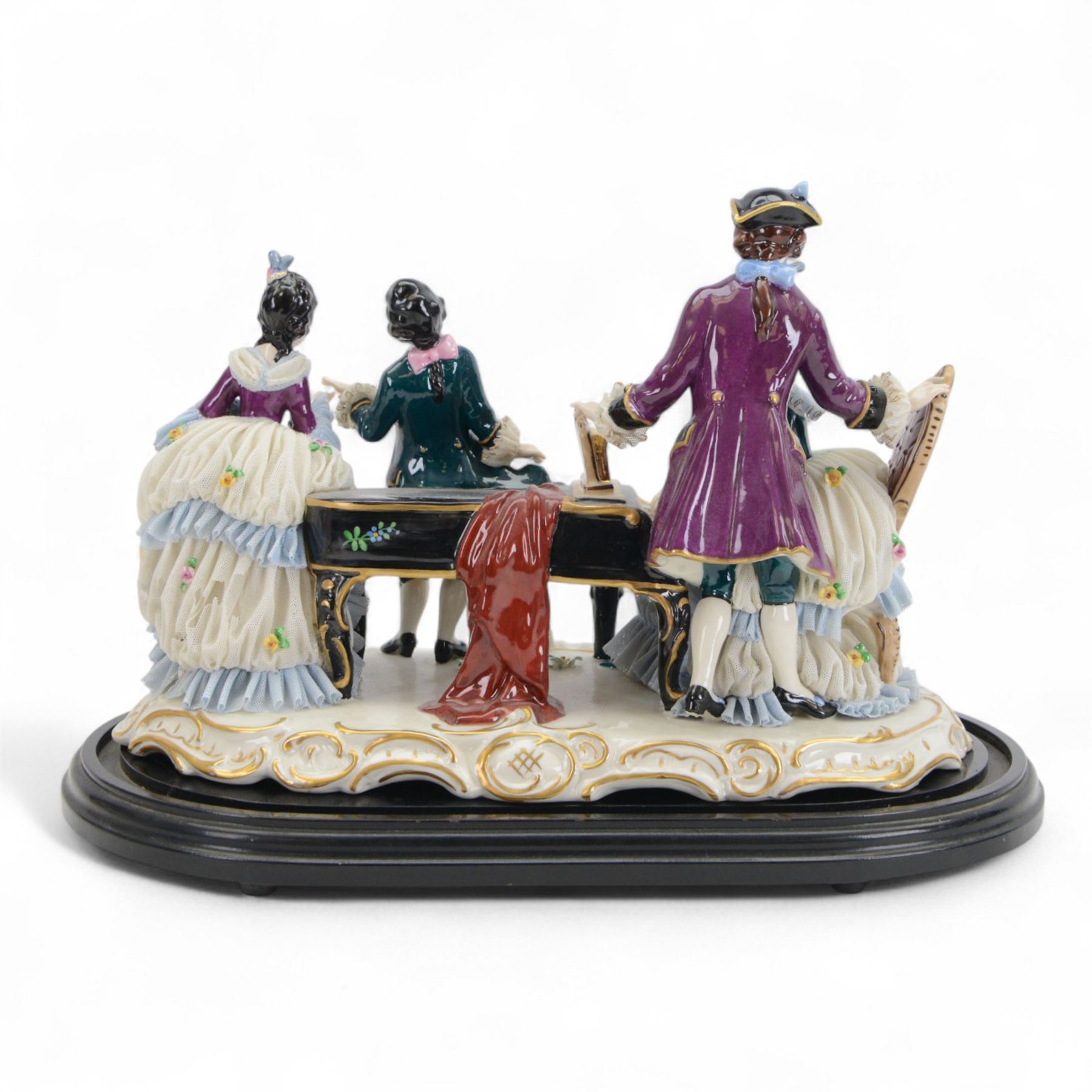German lace figure group, modelled as a piano recital, the female figures with lace skirts and trimmed gowns, the male figures with lace cuffs and cravats, upon a gilt scrolling base, H22.5cm W33cm 