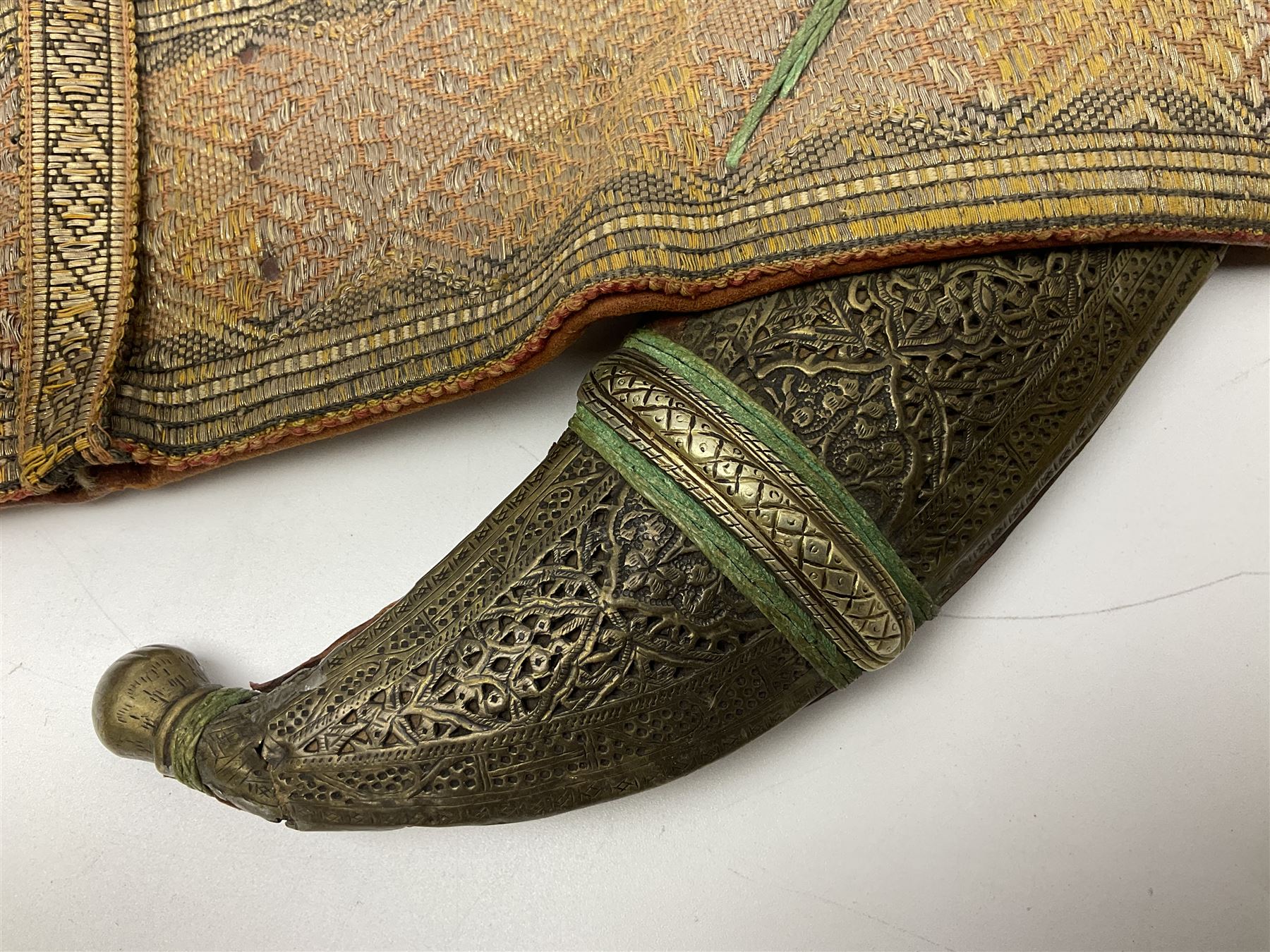 Late 19th century Yemeni Tuza jambiya as worn by religious elite, the 20.5cm curving blade with raised medial ridge, the horn hilt with pique style studwork, in a leather wrapped wooden scabbard with pierced metal mount and leather belt applied with embroidered 'gold' and 'silver' thread work panel; dagger L36cm overall, belt L84cm