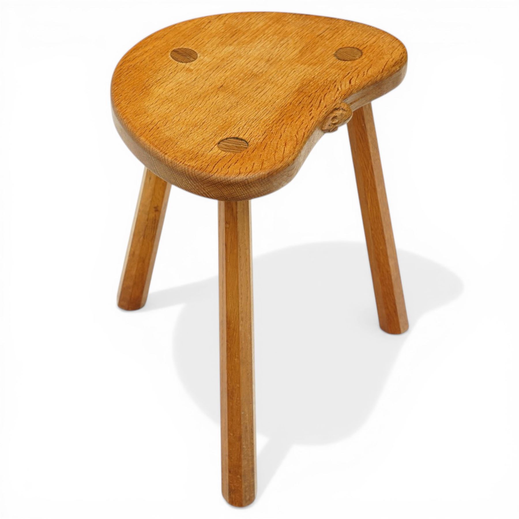 Mouseman - oak three-legged stool, dished kidney-shaped seat, raised on three octagonal splayed supports, with carved mouse signature, by the workshop of Robert Thompson of Kilburn