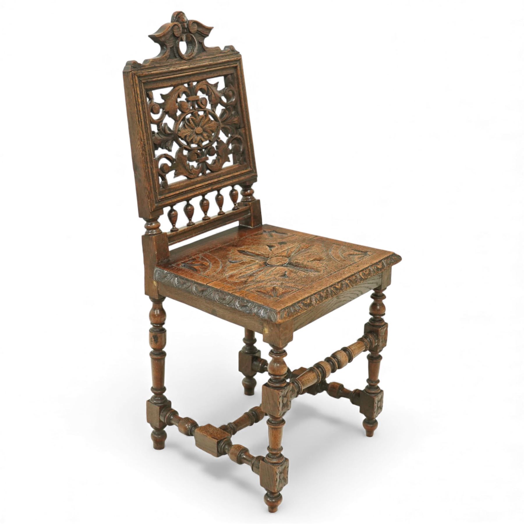 18th century carved oak hall chair, the rectangular pierced back carved with scrolling foliate ornament and central rosette beneath a shaped cresting, the boarded seat carved with stylised foliage, raised on turned legs united by stretchers