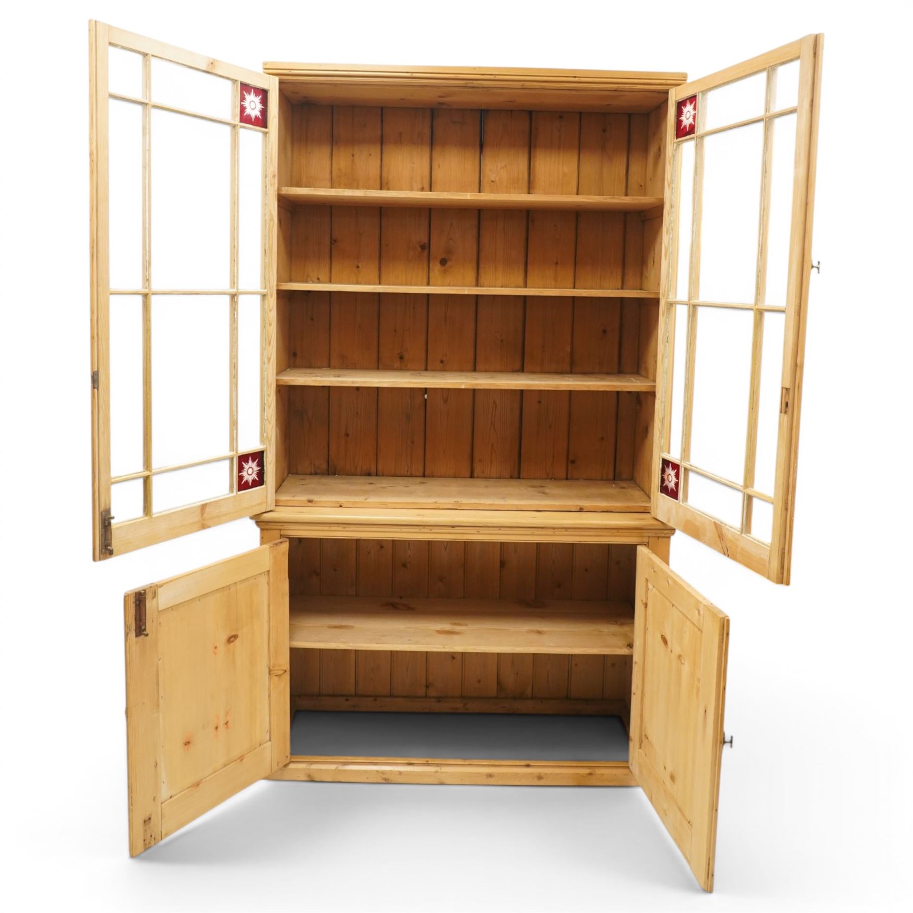19th century pine glazed bookcase cupboard, twin astragal glazed doors with stained glass corner panels, enclosing fixed shelves, the lower section fitted with two panelled cupboard doors enclosing single shelf, on plinth base