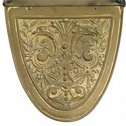 Late 19th century brass coal scuttle, of helmet form, with embossed scrolling foliate panels, cast iron supports with turned ebonised handle, raised on a cast iron tripod base