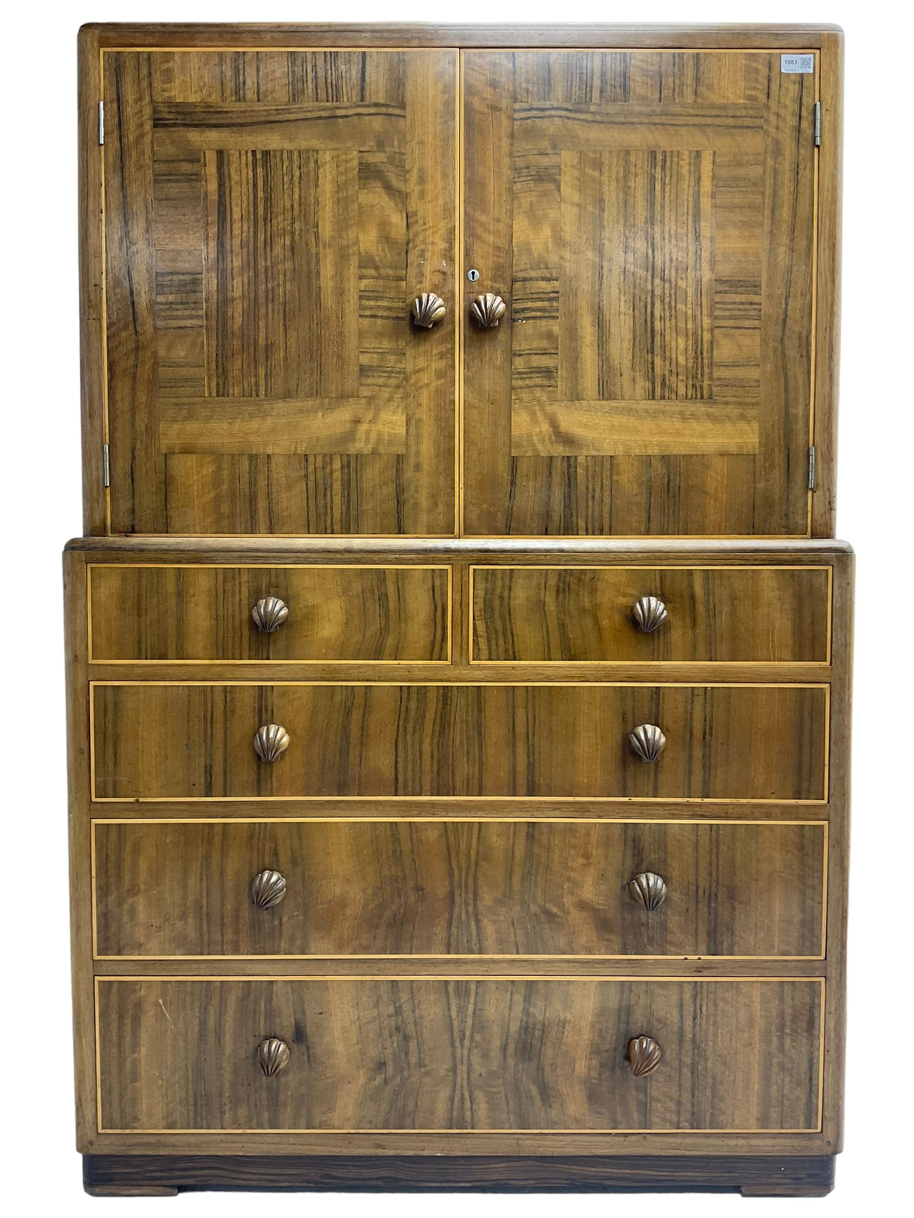 Early 20th century Art Deco walnut cocktail tallboy chest, fitted with double cupboard enclosing two shelves over two short and three long drawers, each with shell shaped handes