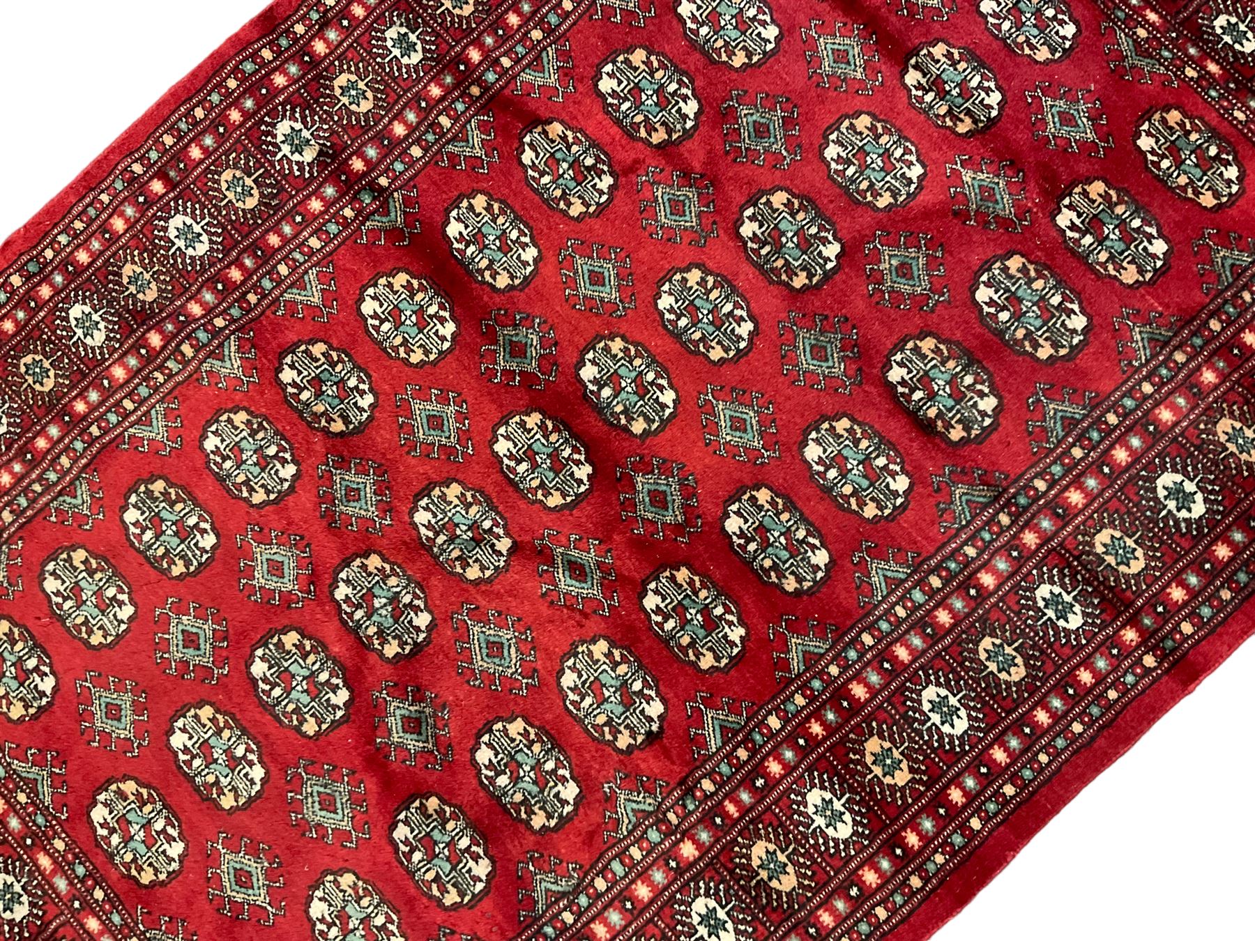 Persian Bokhara crimson ground rug, the field decorated with repeating Gul motifs and lozenges, the multi-band border with stylised plant motifs with black outlines