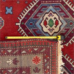 Caucasian Kazak rug, red field decorated with a column of stepped hexagonal medallions in blue, ivory, and crimson, flanked by stylized floral and geometric motifs, enclosed by multiple borders of rosettes and hooked designs 
